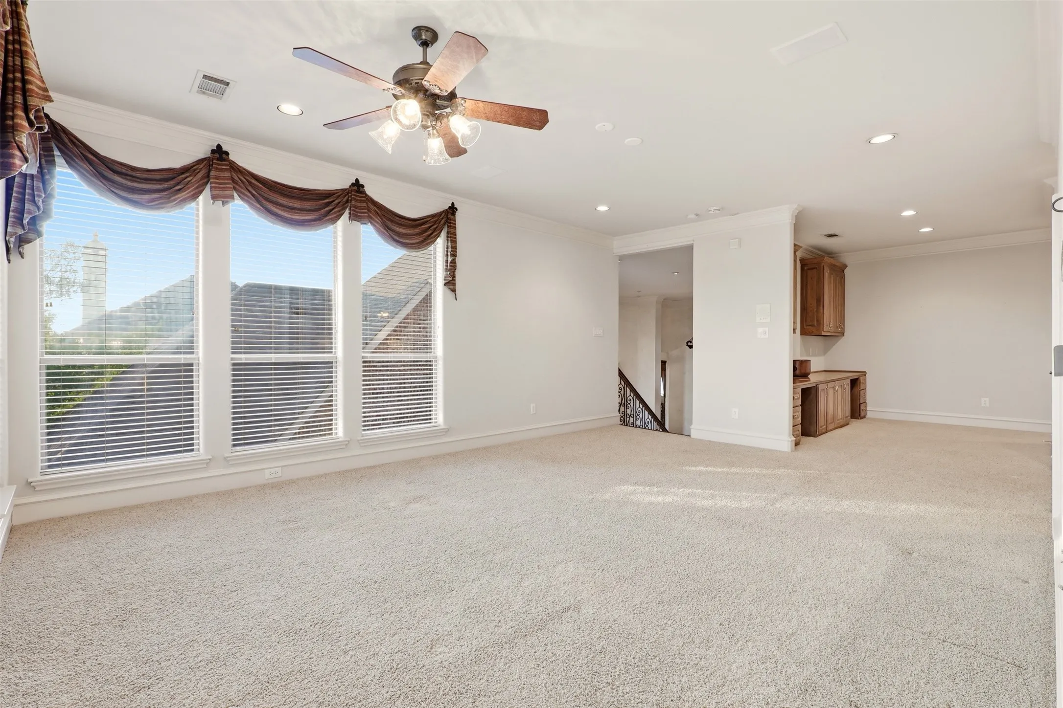 Expansive carpeted area featuring a ceiling fan with integrated lighting, recessed lighting, and a built-in desk with cabinetry