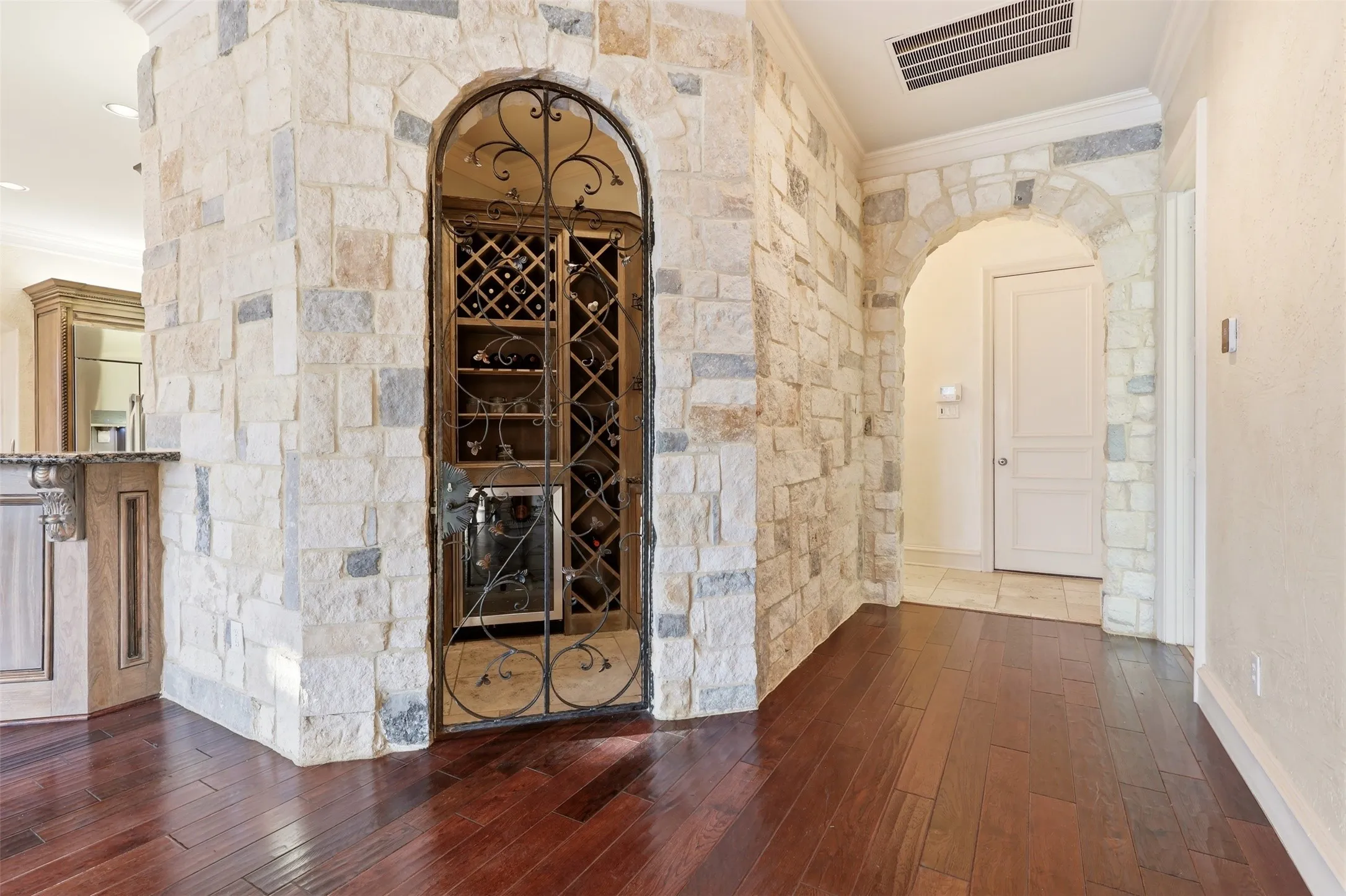 Stone accent wall with an arched entryway and a built-in wine cellar featuring a wrought iron gate