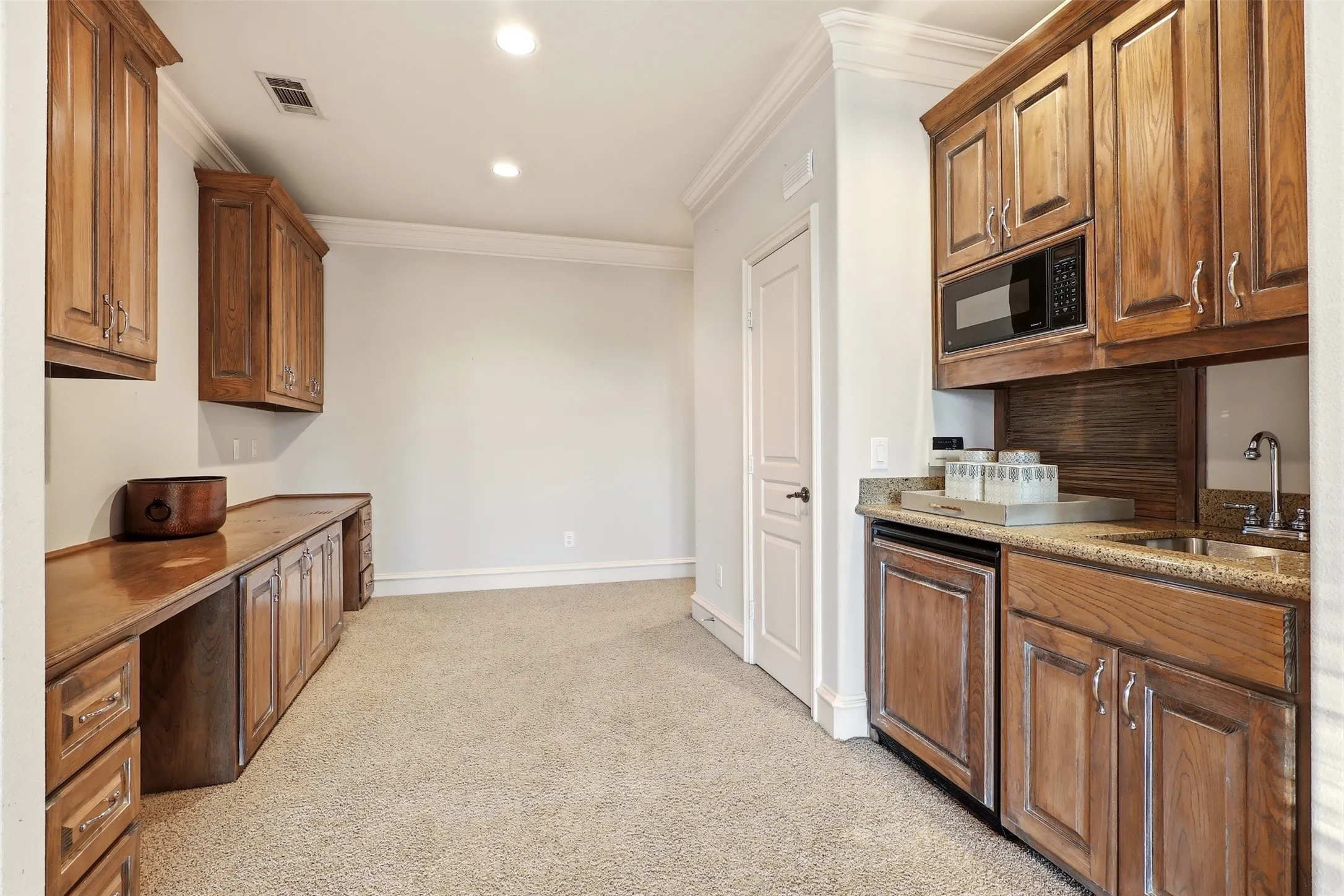 Built-in cabinetry with wood-finish, recessed lighting, crown molding, integrated microwave, and a wet bar with a sink