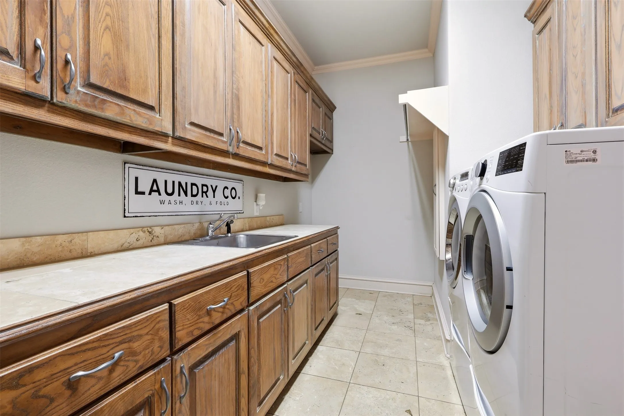 Wood-finish cabinetry, tile countertops with integrated sink, tile flooring, and integrated clothes hanging rack and room for Freezer or Refrigerator