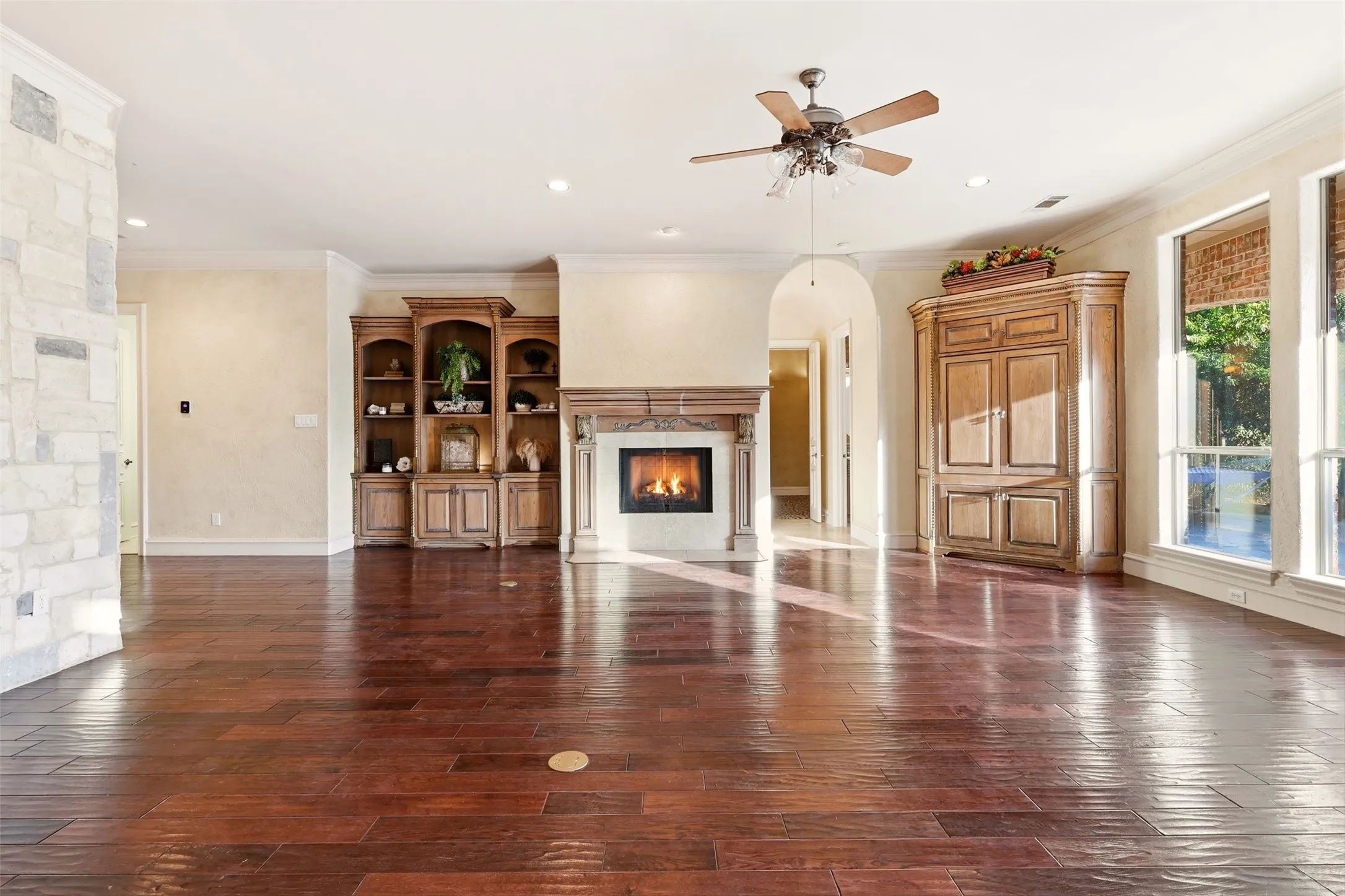 Hardwood flooring, stone accent wall, decorative fireplace with mantel, built-in cabinetry, and ceiling fan with lighting