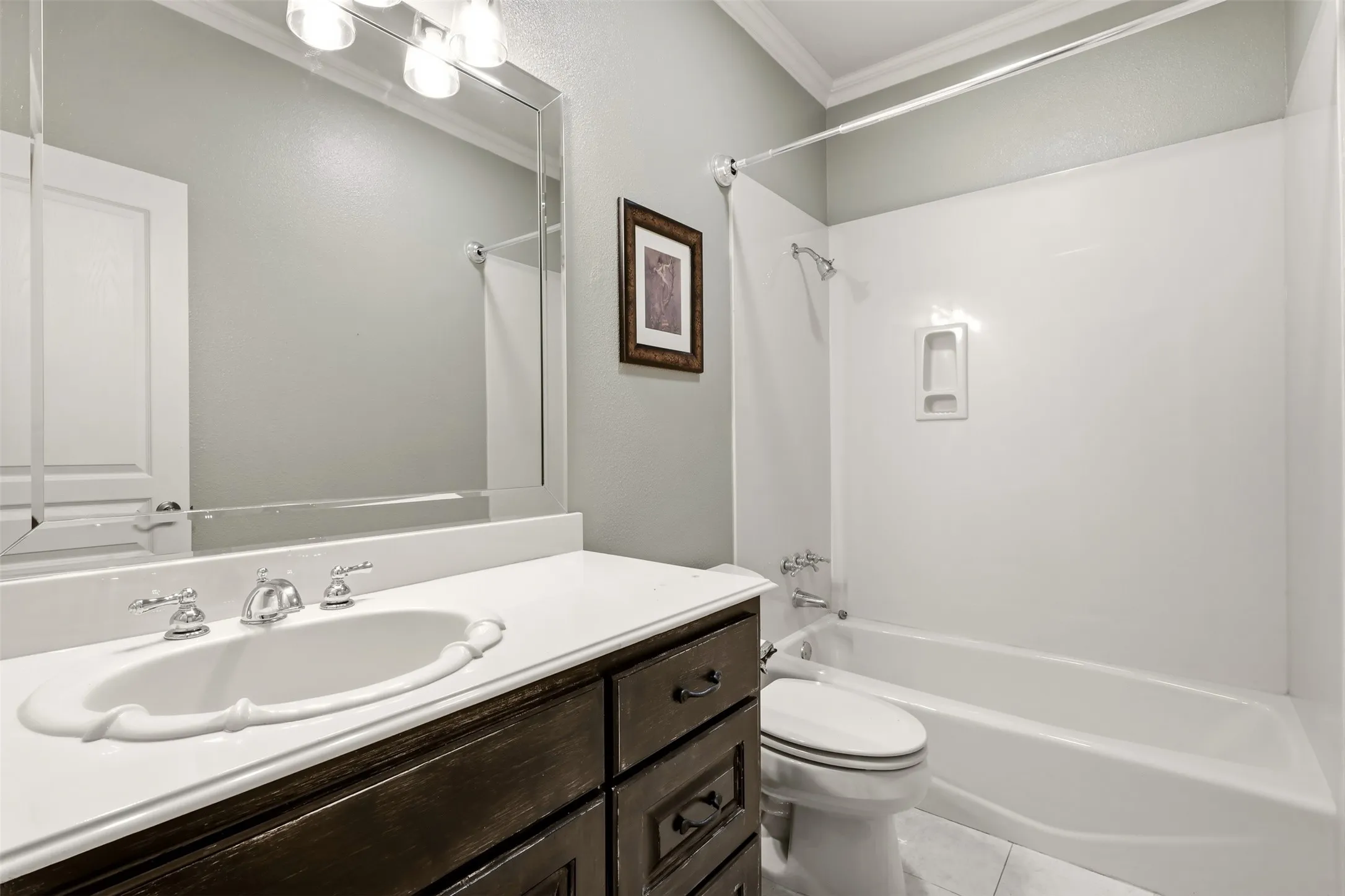 White ceramic vanity sink with chrome fixtures, dark wood-finish cabinetry, light countertop, and a white bathtub with shower