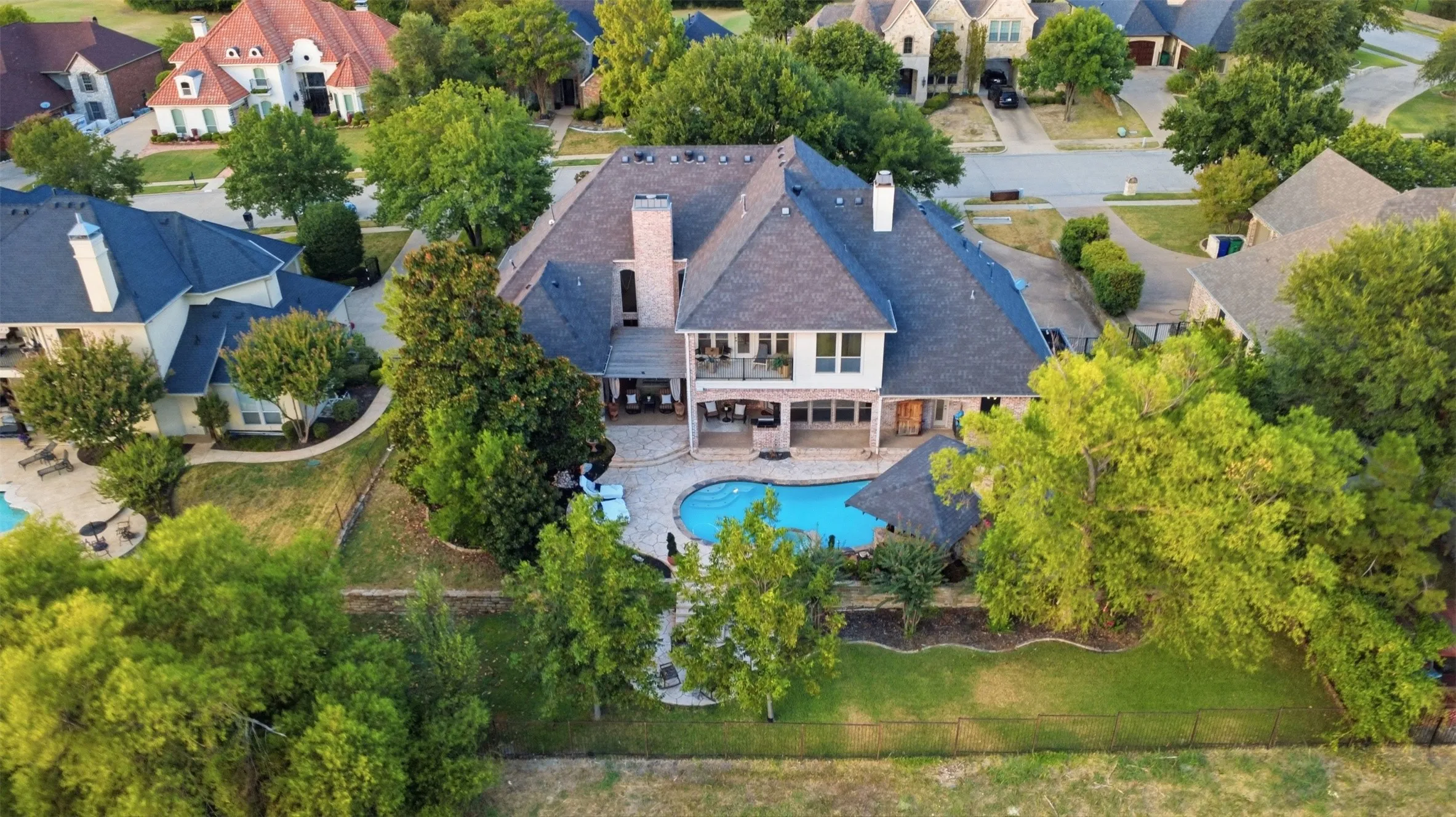 Expansive rear exterior featuring a swimming pool, covered patio, second-story balcony, and mature trees. This home backs up to the green belt for privacy. The custom details enhances the view as the sun sets around it.