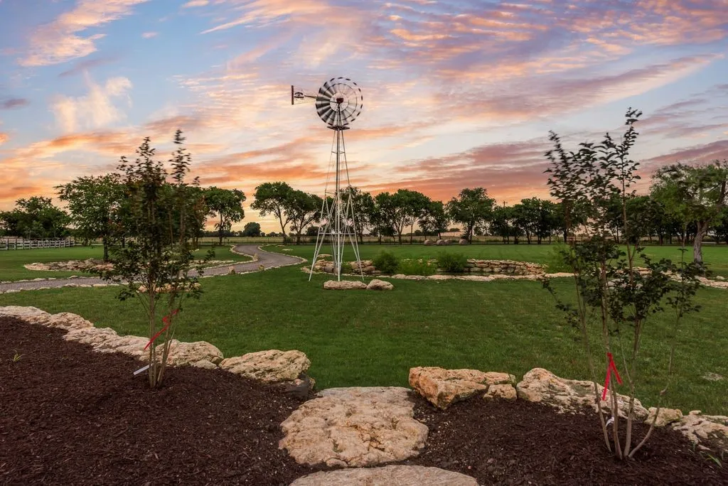 Expansive green space featuring a decorative windmill, meandering paved pathways, and mature trees lining the perimeter