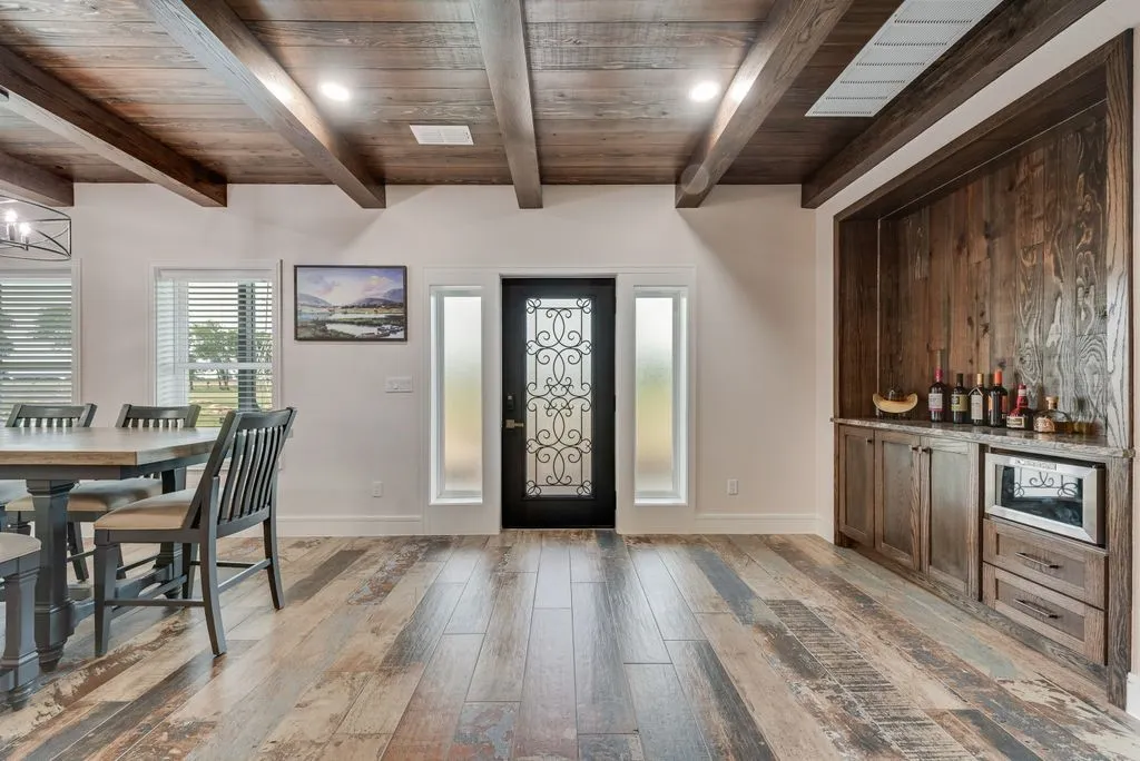 Entryway featuring a decorative wrought iron door, wood-finish flooring, exposed wood beam ceiling, and a built-in beverage bar with wood paneling and stone countertop