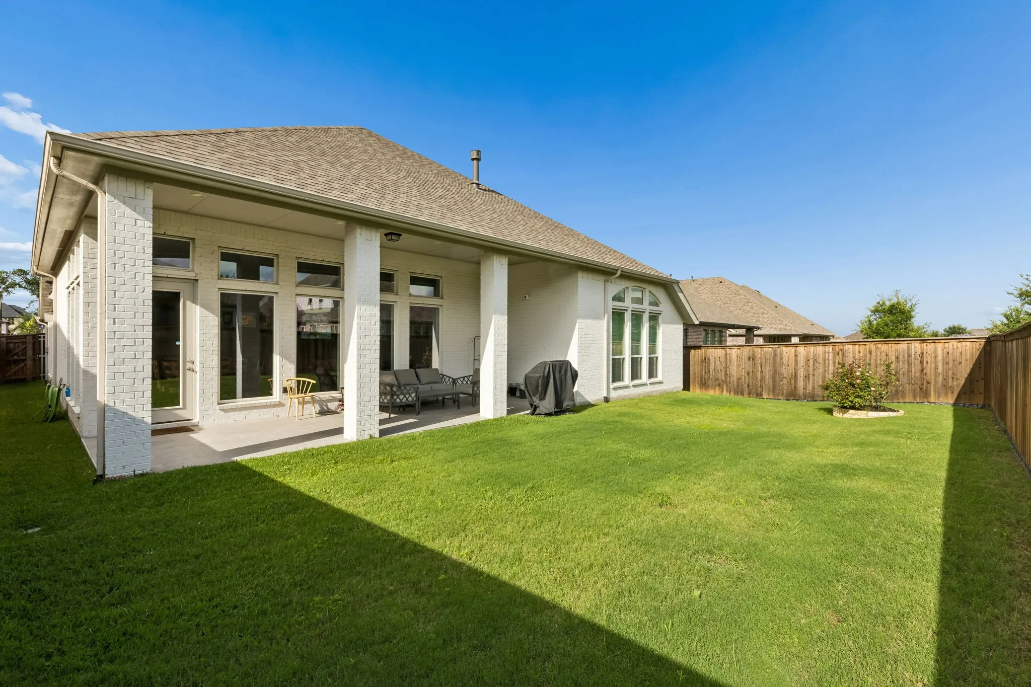Expansive backyard featuring a covered patio, multiple large windows, a fenced perimeter, and a central lawn area
