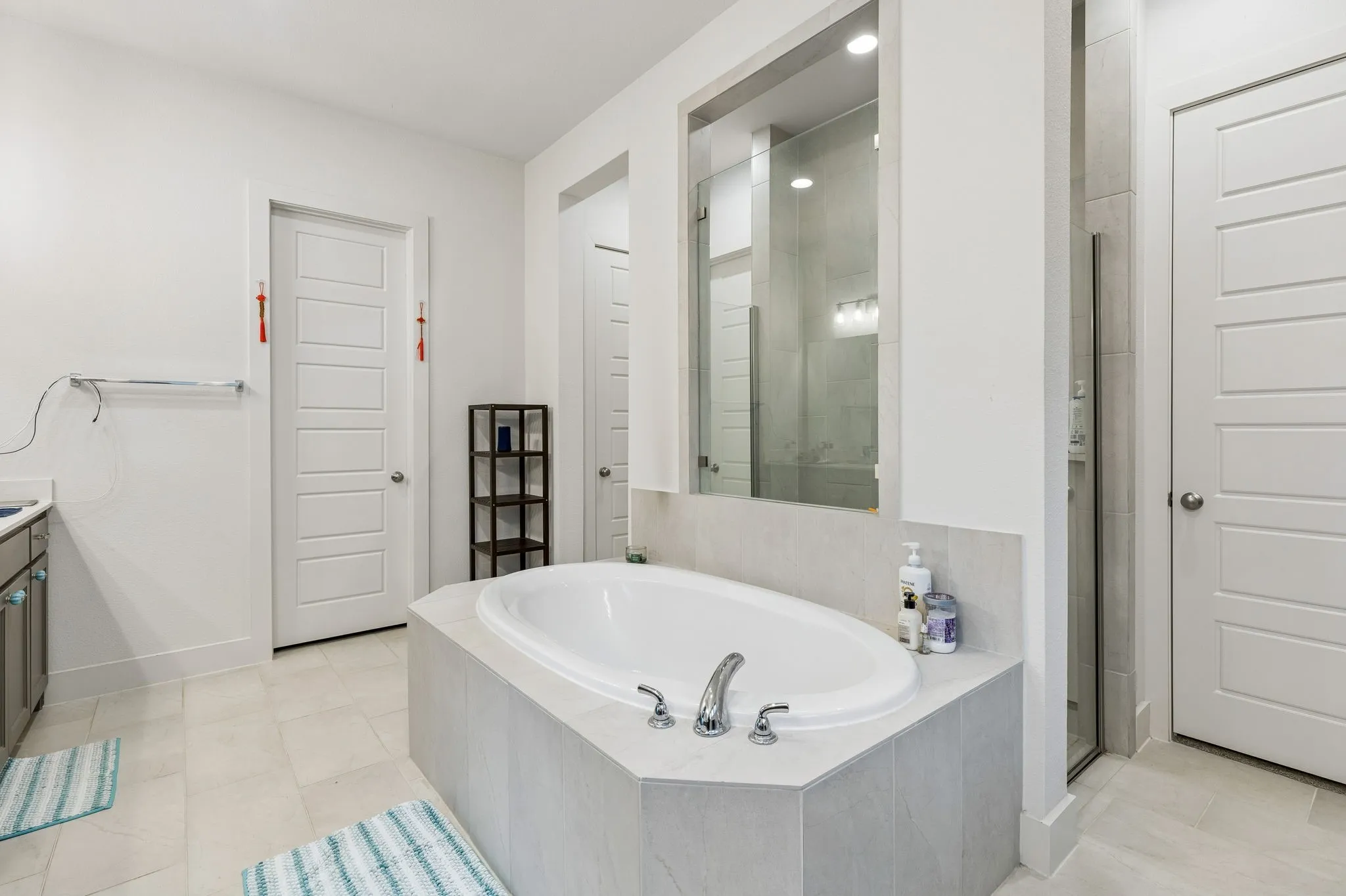 Contemporary bathroom featuring an oval soaking tub with deck-mounted fixtures, a glass-enclosed shower, and light-toned tile flooring