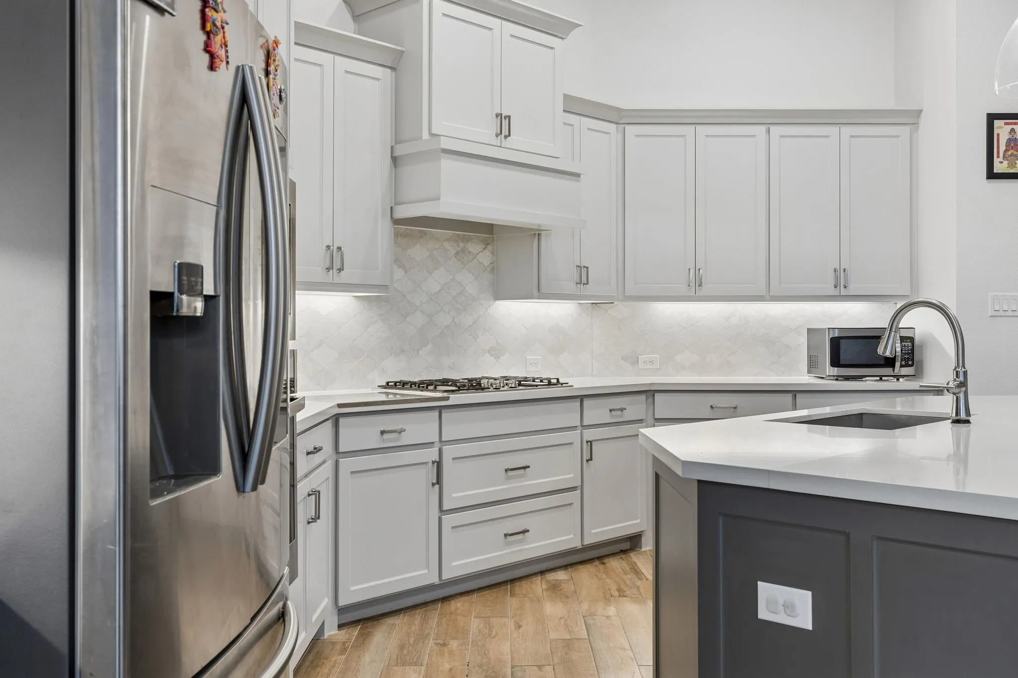 Modern kitchen featuring light gray cabinetry, stainless steel appliances, a gas cooktop, and a kitchen island with an undermount sink