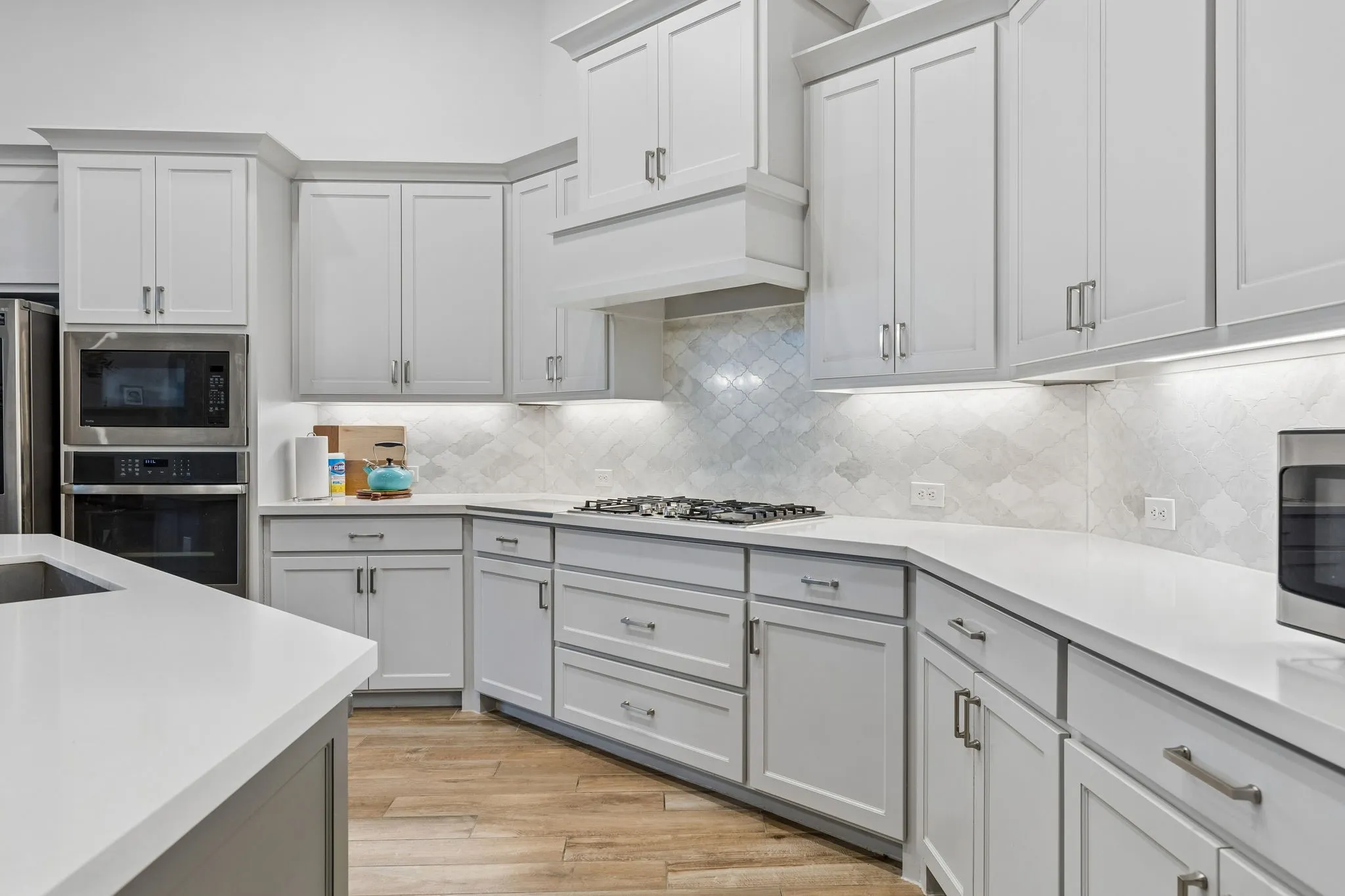 Modern kitchen featuring light gray cabinetry, built-in stainless steel appliances, white countertops, a decorative tile backsplash, and wood-finish flooring