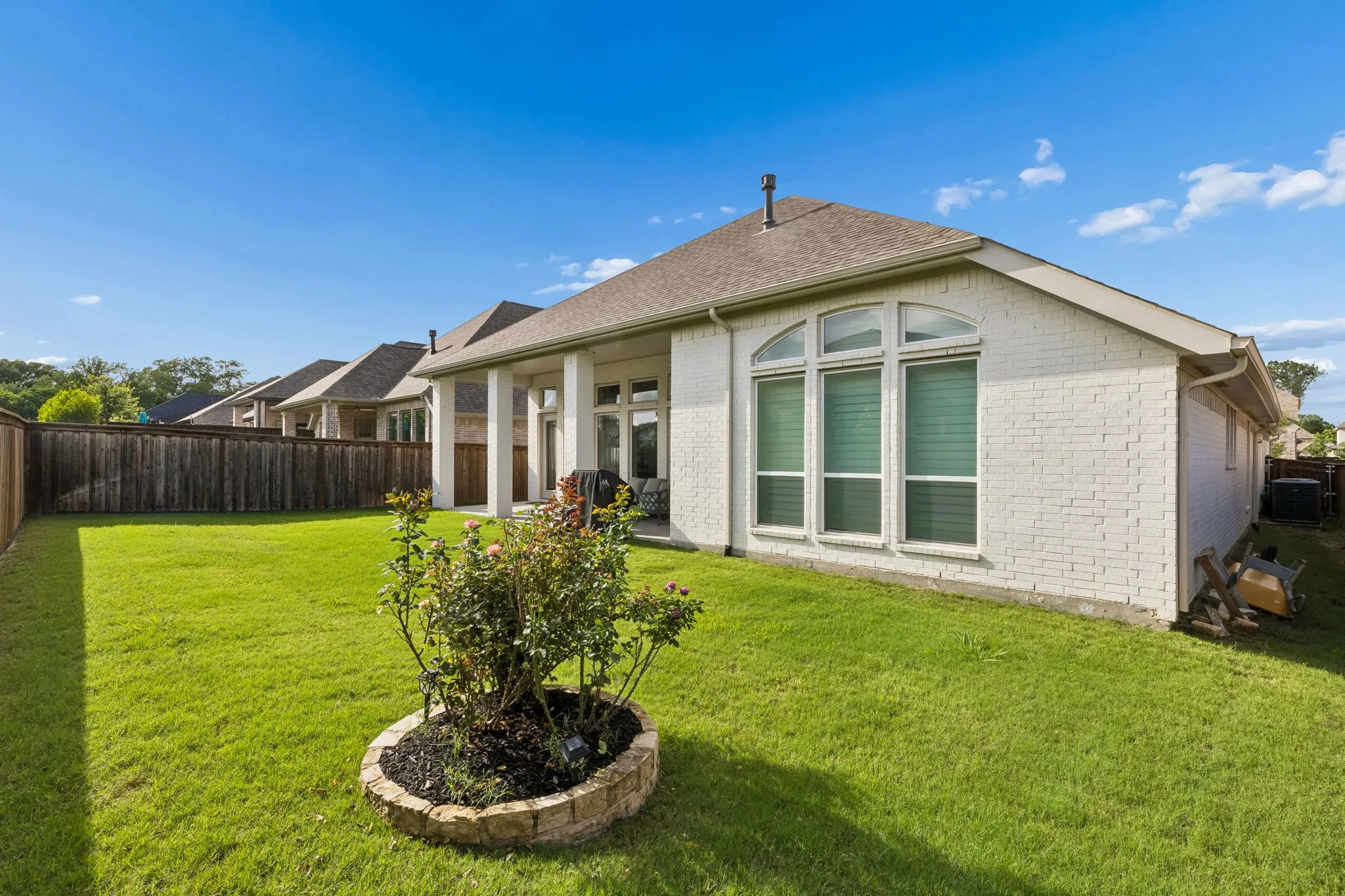 Expansive backyard featuring a lush lawn, privacy fencing, and a decorative garden bed