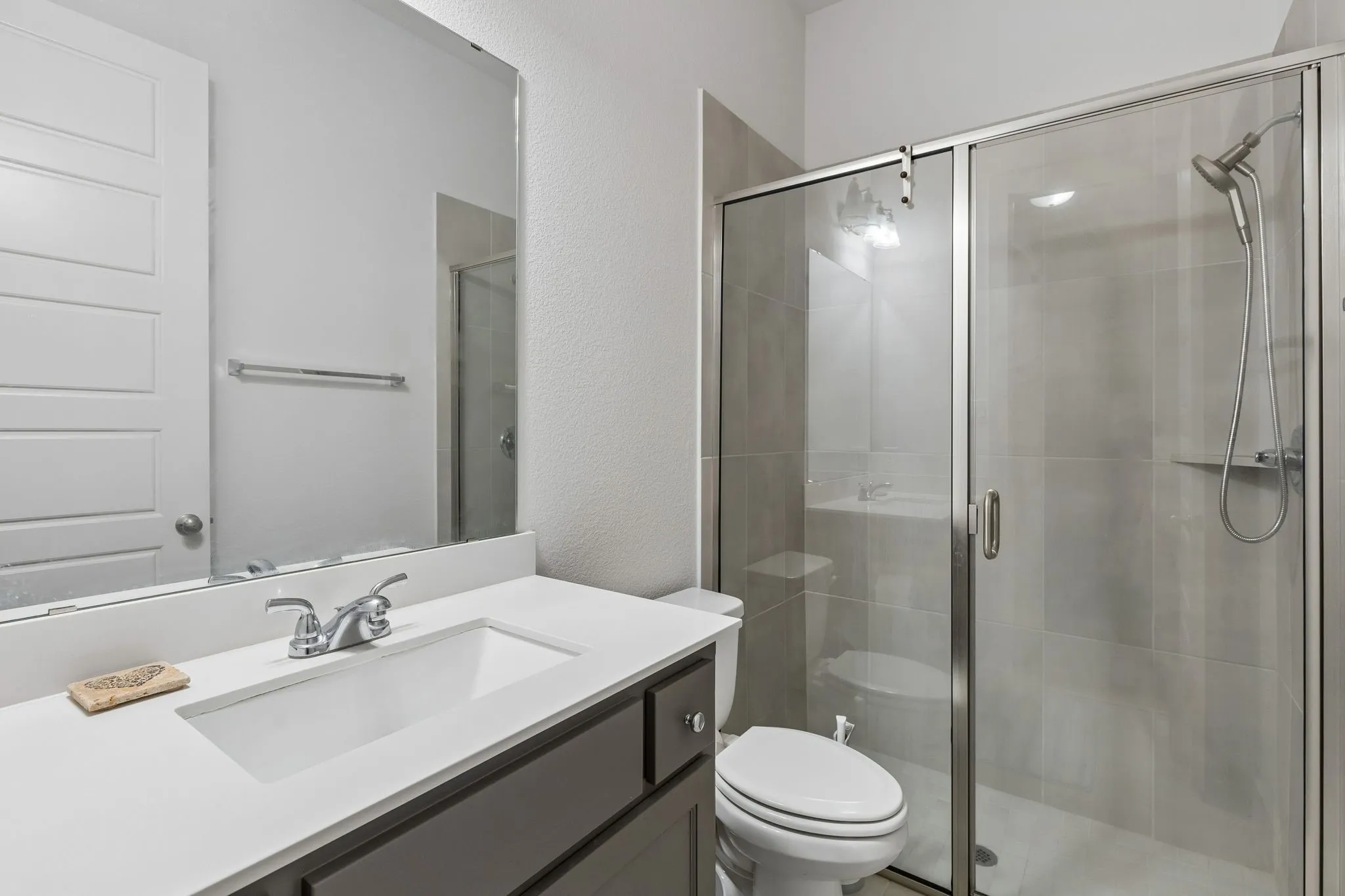 Bathroom featuring a frameless mirror, white vanity countertop, undermount sink with chrome faucet, and a glass-enclosed shower with tiled walls and a handheld showerhead