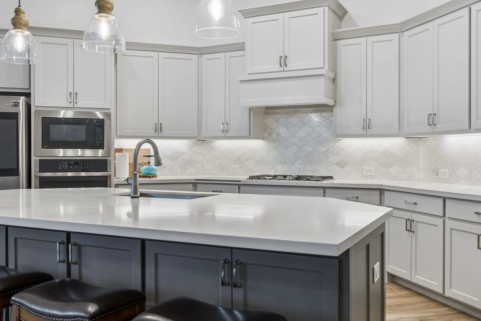 Kitchen featuring a large central island with a sink, light-toned countertops, two-tone cabinetry, stainless steel appliances, and a tiled backsplash