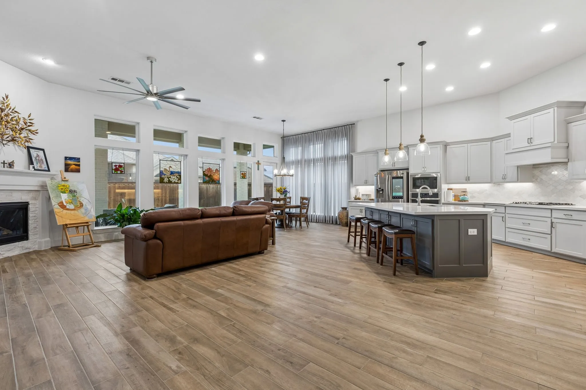 Open-concept living area featuring wood-finish flooring, a modern fireplace with a white mantel, and a ceiling fan
