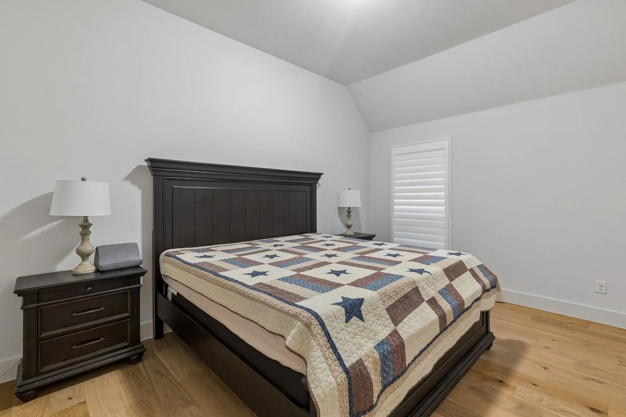 Room featuring wood-finish flooring, white walls, and a window with white louvered shutters