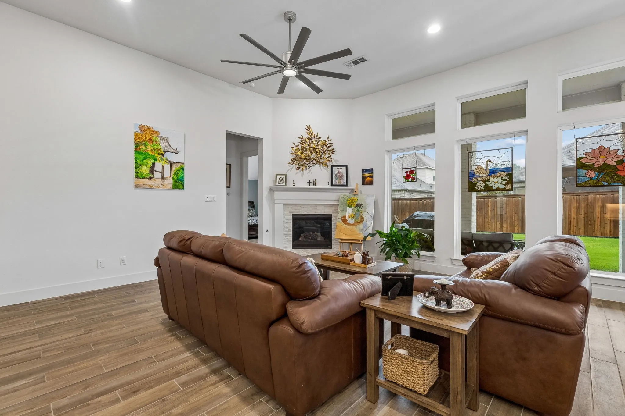 Living area featuring wood-finish tile flooring, a corner fireplace with a white mantel, and a multi-blade ceiling fan
