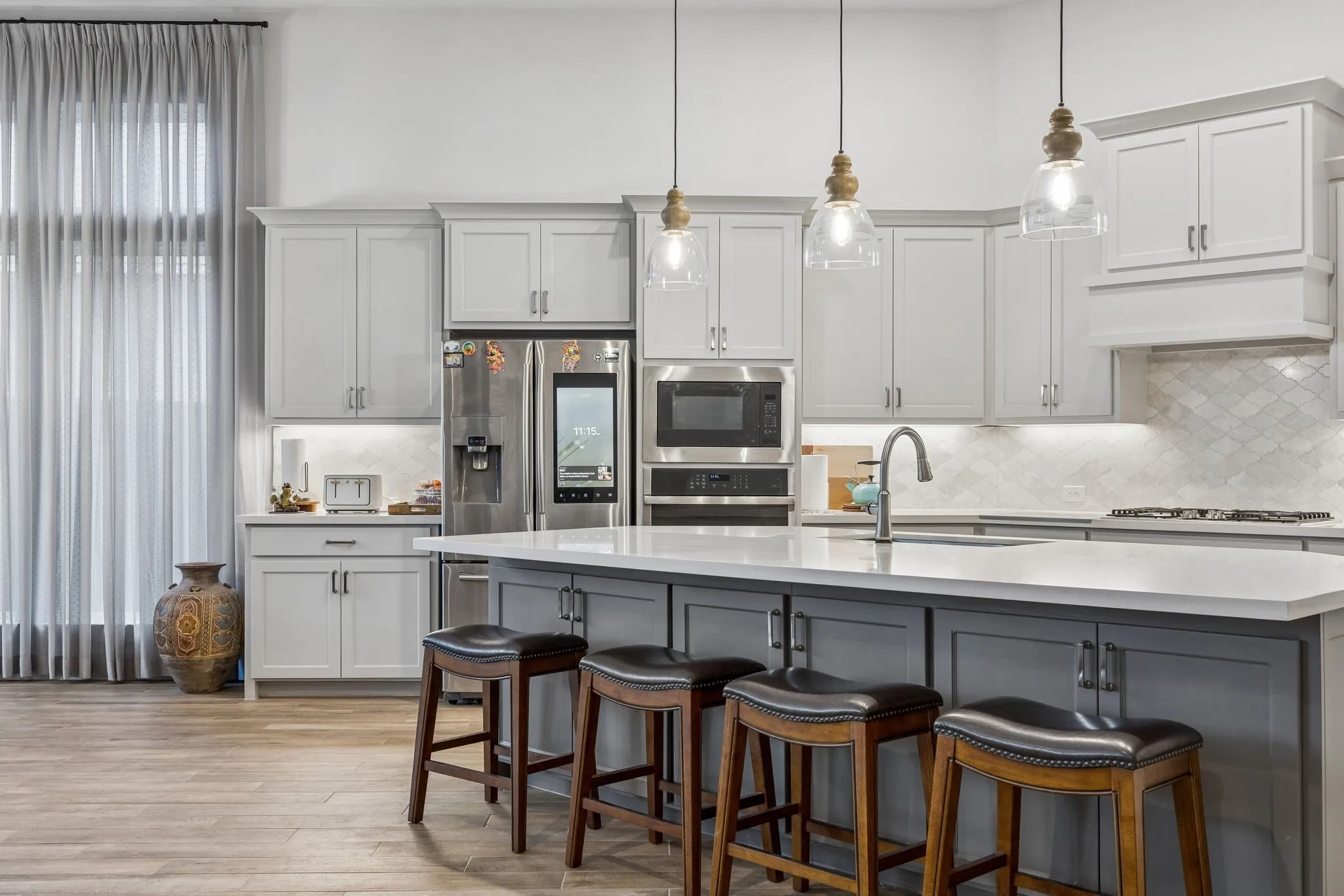 Spacious kitchen featuring a large central island with seating, stainless steel appliances, light cabinetry, a patterned backsplash, and wood-finish flooring