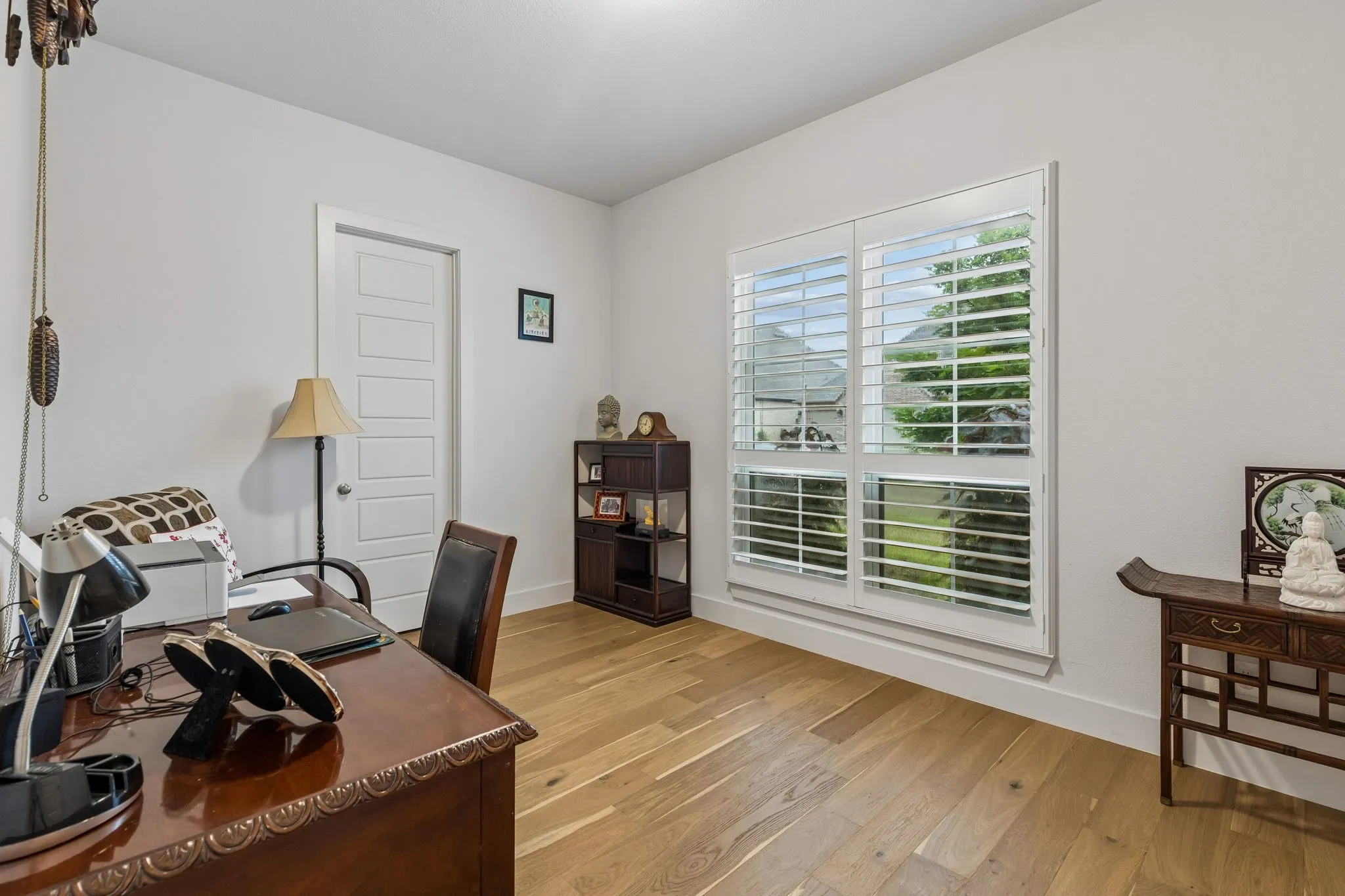Bright room featuring hardwood flooring, white walls, and a multi-panel window with white plantation shutters