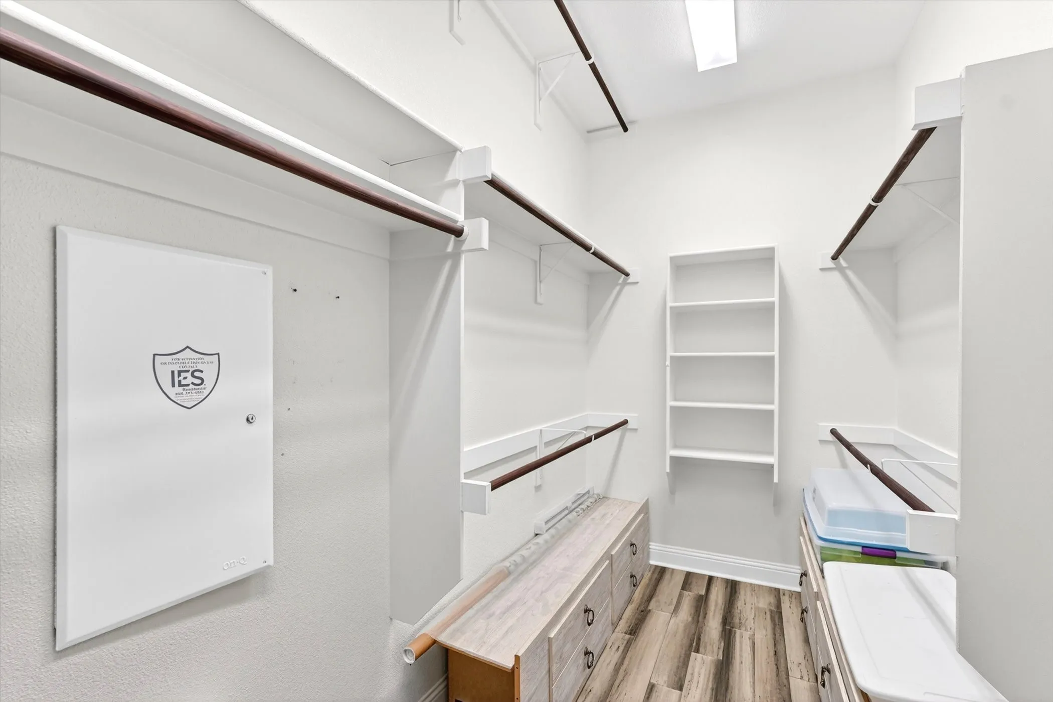 Spacious walk-in closet featuring custom shelving, dual hanging rods, and built-in cubbies for organized storage. The two lower drawer units are freestanding and can be removed to suit the new owner's preferences.