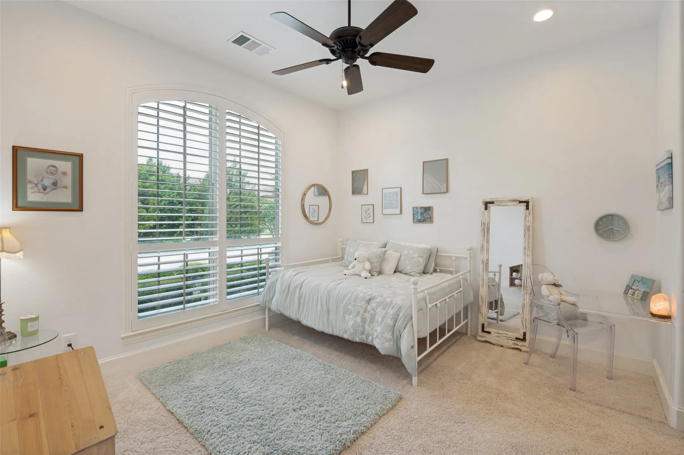 This oversized secondary bedroom offers a private and comfortable retreat, featuring generous dimensions that easily accommodate larger furnishings while still providing plenty of open space. A dramatic arched window adorned with plantation shutters floods the room with natural light, while plush carpeting, and soaring ceilings enhance the sense of warmth and spaciousness, making this room ideal for family members or guests. the bedroom includes a private ensuite bath, providing convenience, comfort, and an elevated level of privacy and walk-in closet.