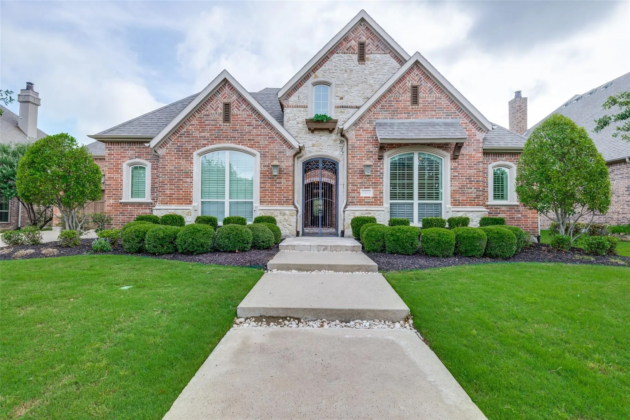 Welcome to refined luxury living in the gated village of The Tribute Lakeside Resort & Golf Community. A charming arched entry with an elegant iron front door creates a warm and inviting first impression, while mature trees and meticulously trimmed hedges frame the home with sophistication.