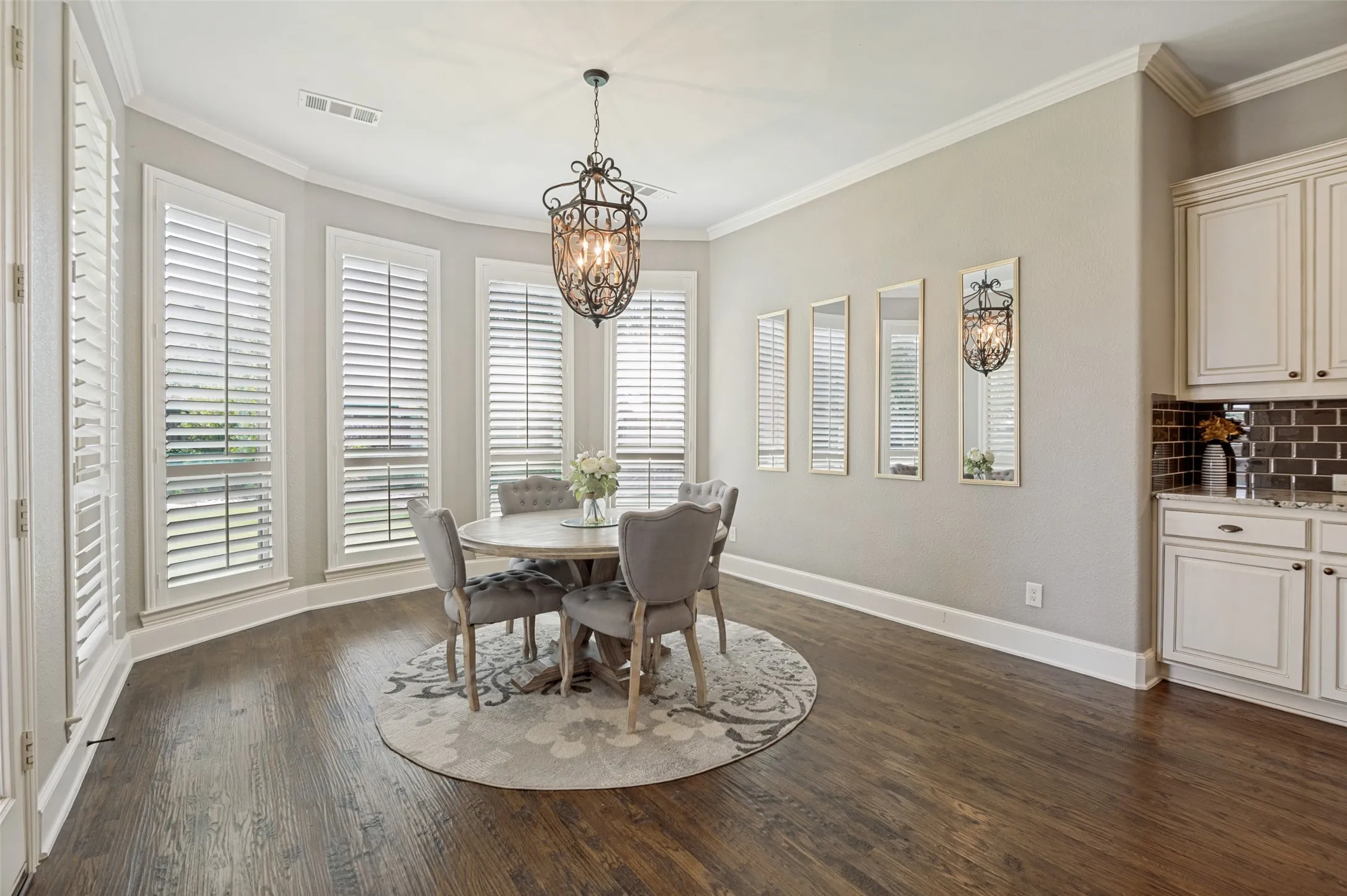 Bathed in natural light, this spacious breakfast room offers a warm and inviting setting for everyday dining. A wall of oversized windows adorned with classic plantation shutters creates a bright, airy atmosphere while providing beautiful views and timeless elegance.