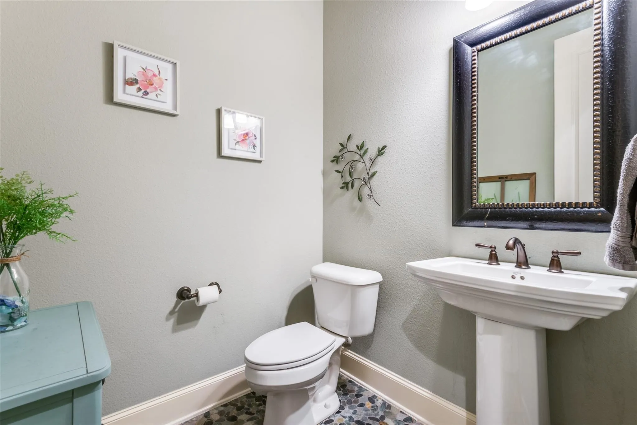 This charming half bath combines style and convenience, offering guests a warm and welcoming experience. A classic pedestal sink, elegant framed mirror, and designer fixtures create a timeless aesthetic, while the unique pebble-style flooring adds character and visual appeal.