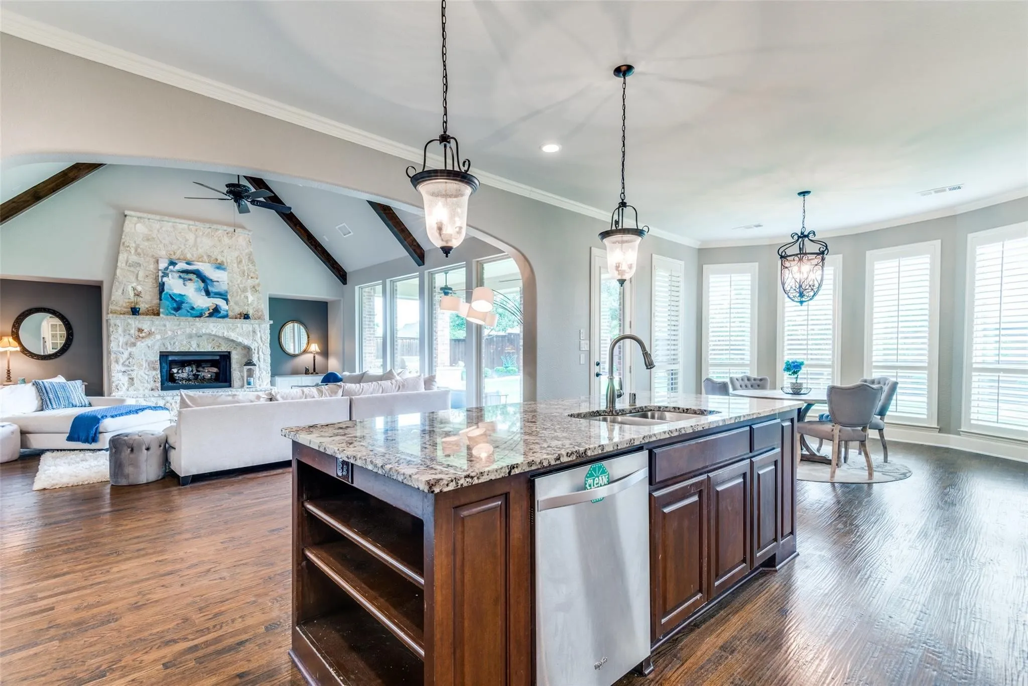 Designed for both everyday living and effortless entertaining, this grand open-concept space seamlessly blends the kitchen, dining, and living areas into one breathtaking gathering place. Rich hardwood floors, soaring ceilings accented by exposed wood beams, and walls of windows create an atmosphere that feels both expansive and inviting. The oversized island anchors the space, offering the perfect spot for casual dining, meal preparation, or conversation with guests.