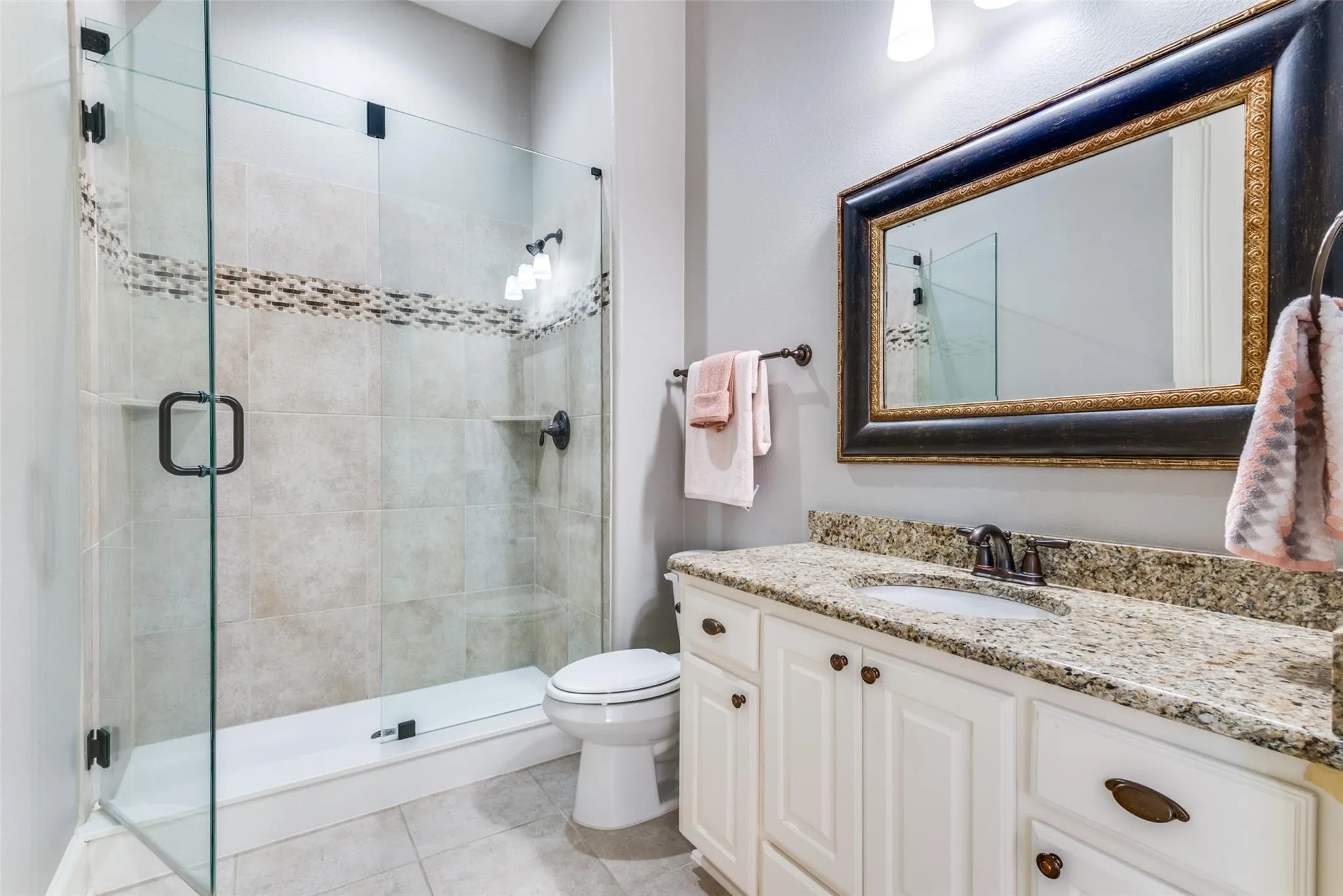 This ensuite bath offers a spacious granite-topped vanity, ample storage and countertop space, while elegant cabinetry and designer fixtures add a touch of sophistication. The standout feature is the large walk-in shower, complete with a sleek glass enclosure, timeless tile surround, and decorative accent tile that adds visual interest and elegance.