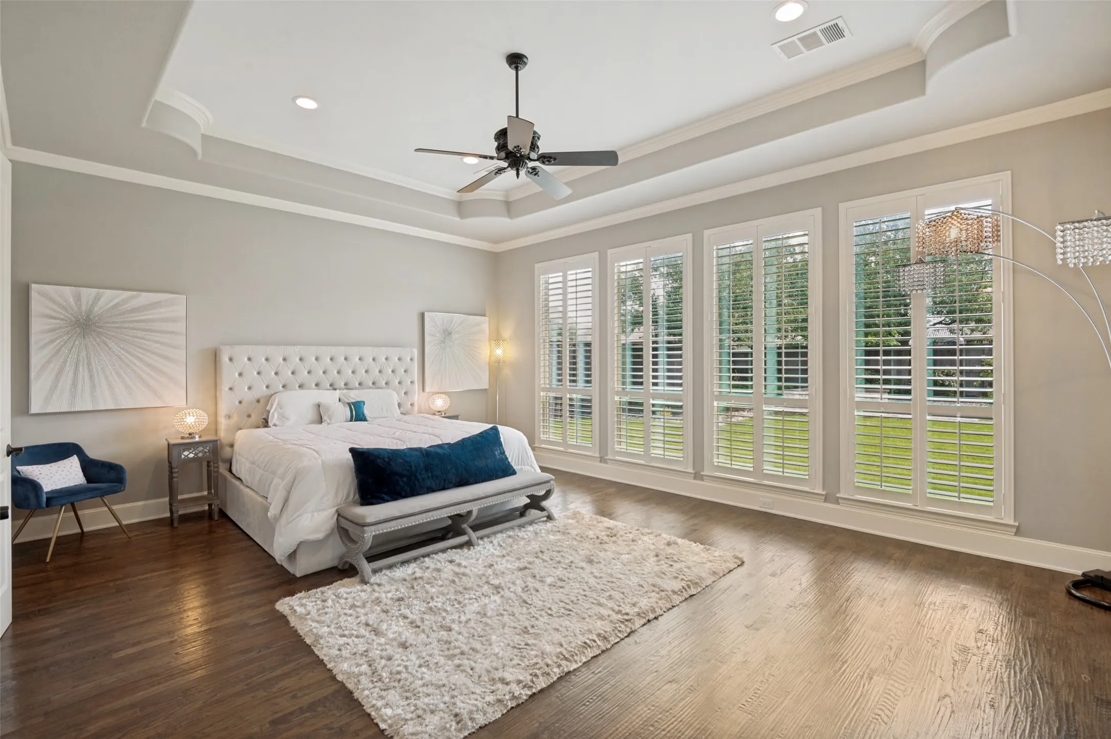 The primary suite is the epitome of luxury, offering a private retreat designed for relaxation and comfort. Soaring tray ceilings with elegant crown molding create a grand sense of scale, while a wall of oversized windows adorned with plantation shutters fills the room with natural light and serene backyard views. Rich hardwood floors add warmth and sophistication, complementing the spacious layout that easily accommodates a private sitting area.