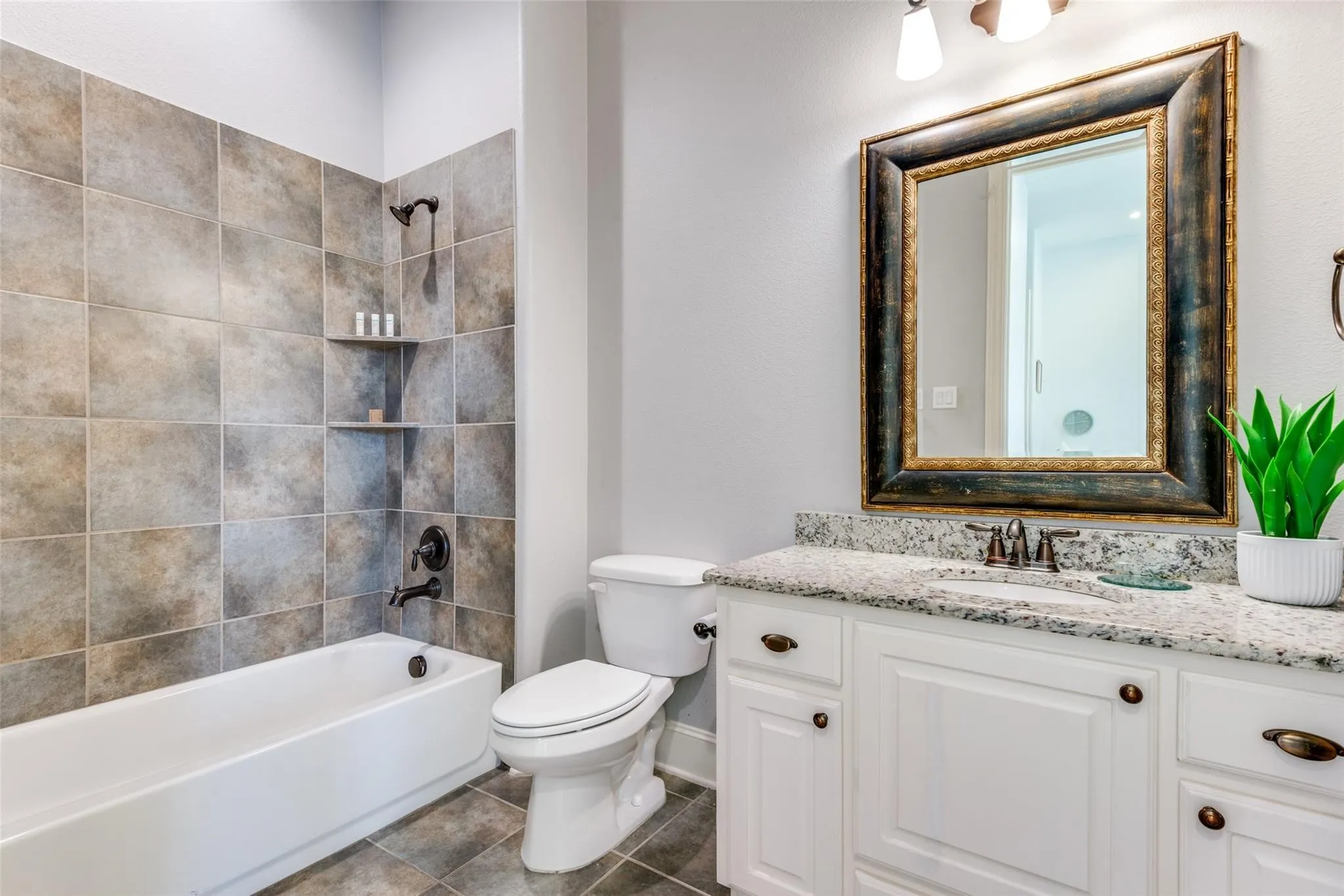 This private ensuite bath is thoughtfully designed with a granite-topped vanity and elegant cabinetry. Timeless finishes and neutral tones offer a sophisticated backdrop that complements any décor. The spacious tub and shower combination is surrounded by beautiful floor-to-ceiling tile, creating a polished and upscale feel while providing the perfect place to unwind after a long day. Conveniently connected to the adjoining bedroom, this well-appointed ensuite bath offers comfort, privacy, and everyday luxury for family members or guests alike.