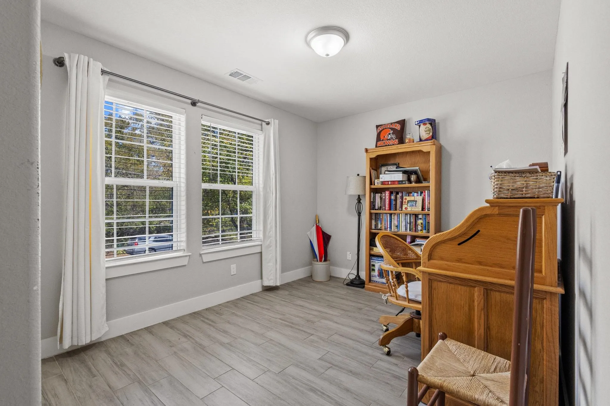 Spacious room featuring two large windows, wood-finish flooring, light gray wall paint, white baseboards, and a flush-mount ceiling light fixture