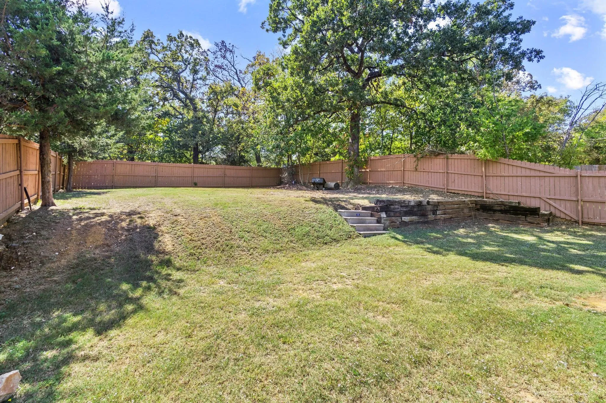 Expansive backyard featuring a tiered landscape, wooden privacy fencing, and mature trees