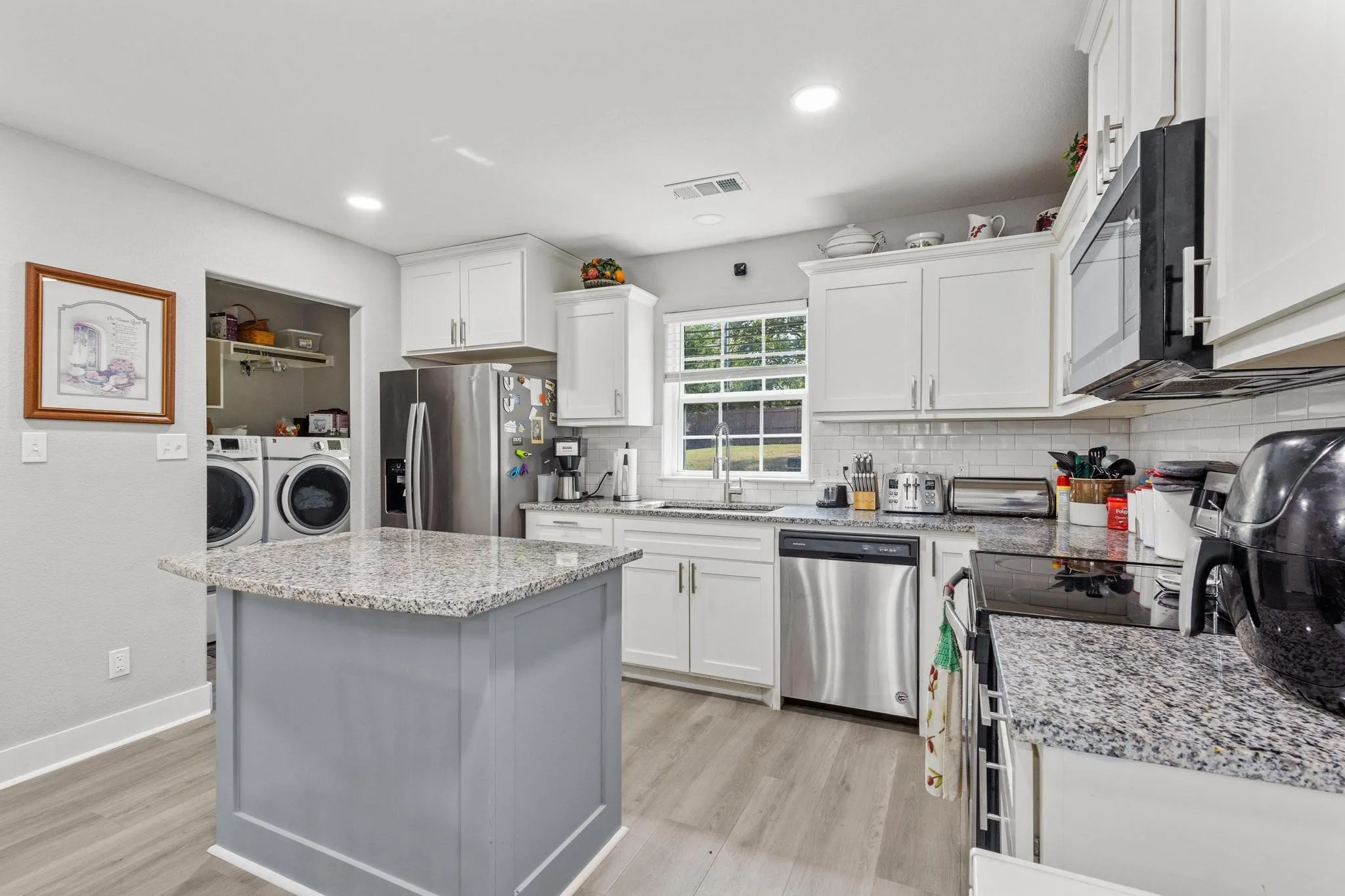 Kitchen featuring white cabinetry, granite countertops, stainless steel appliances, a subway tile backsplash, and wood-finish flooring