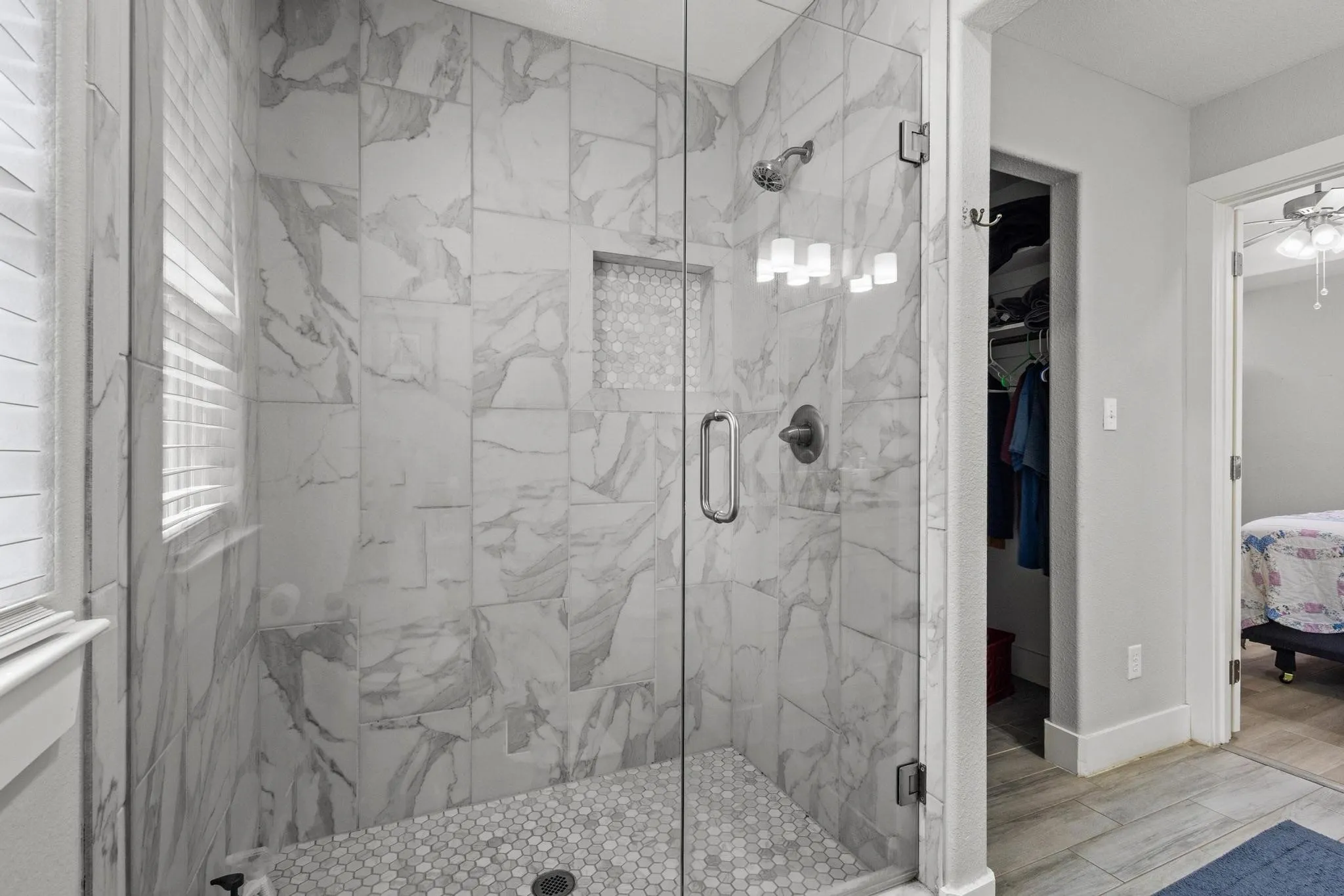 Walk-in shower featuring glass enclosure, marble-style wall tile, hexagonal floor tile, recessed niche, and brushed nickel fixtures