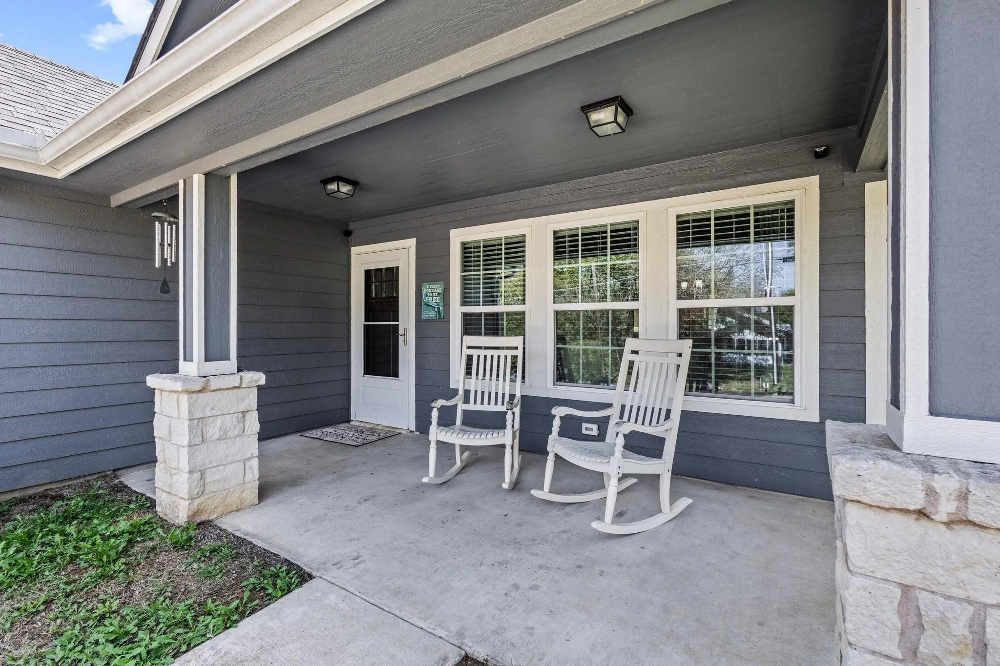 Inviting covered front porch with concrete flooring, accented by stone column bases and a white paneled entry door
