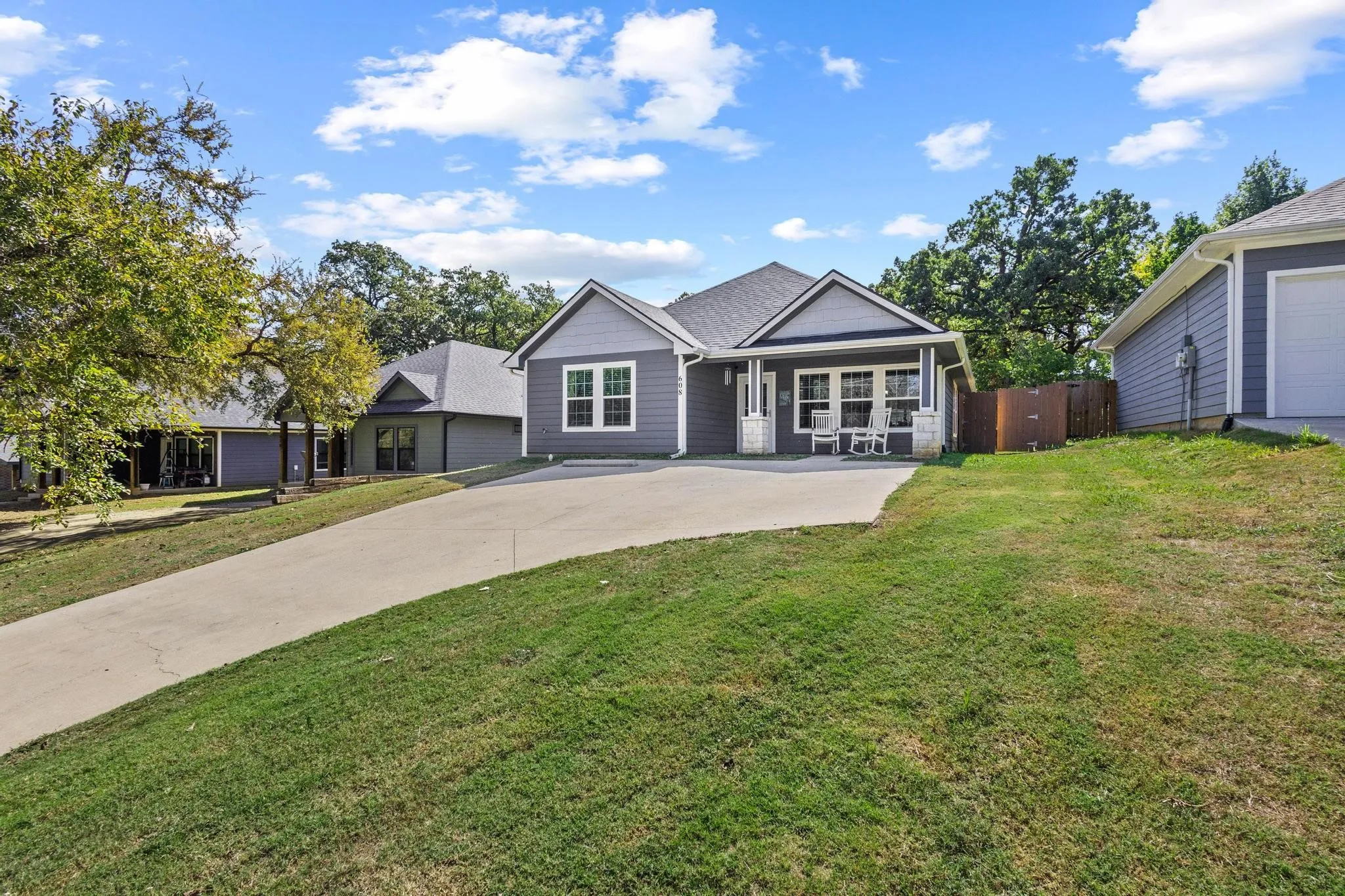 Contemporary residence featuring a dark gray facade with white trim, a covered front porch, an attached garage, a concrete driveway, and established landscaping