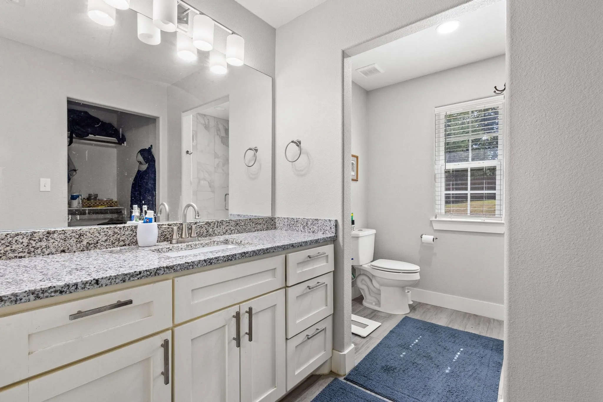 Double vanity featuring a light granite countertop and white shaker-style cabinetry with brushed nickel hardware
