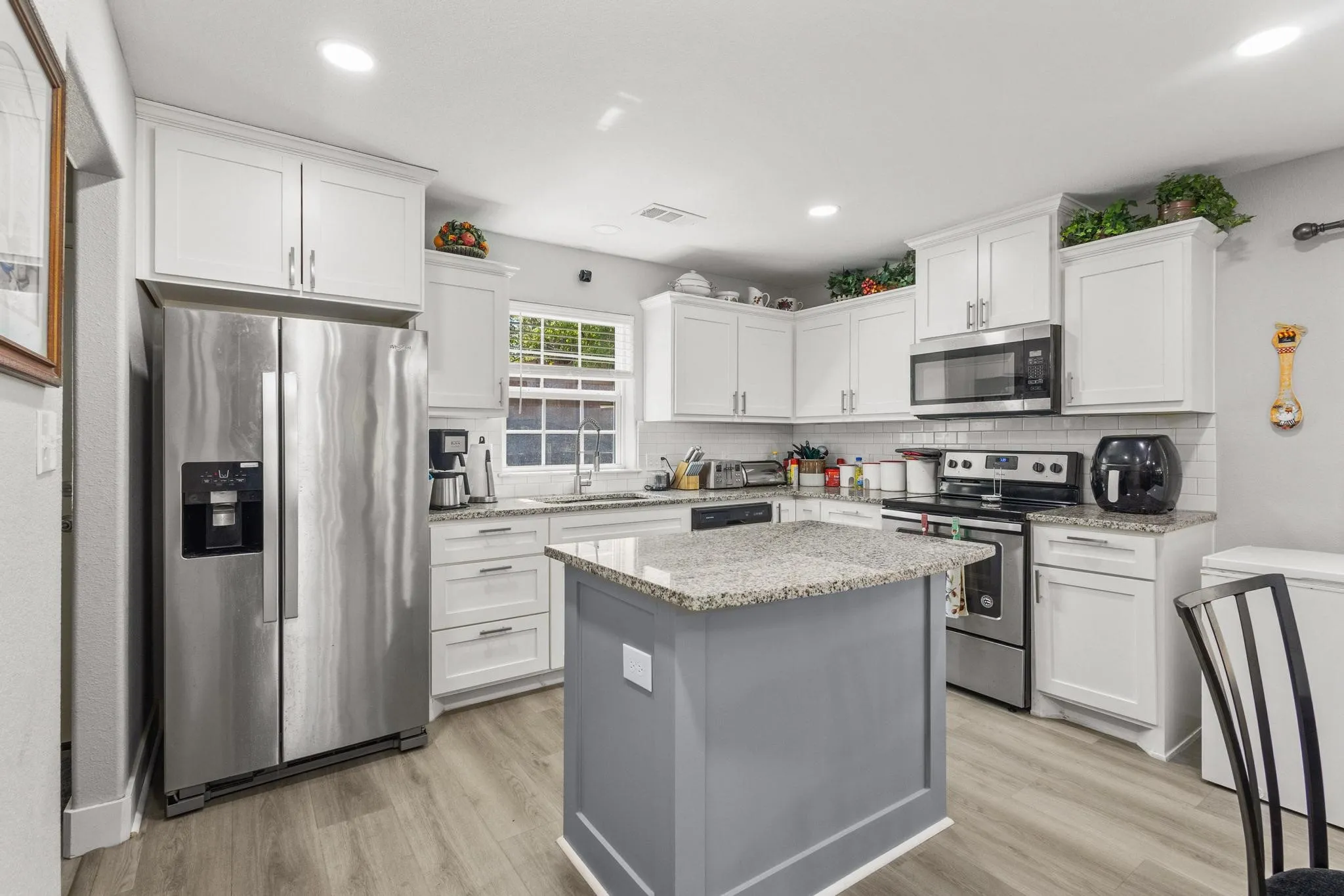 Kitchen featuring a central island with a granite countertop, white cabinetry, stainless steel appliances, and wood-finish flooring