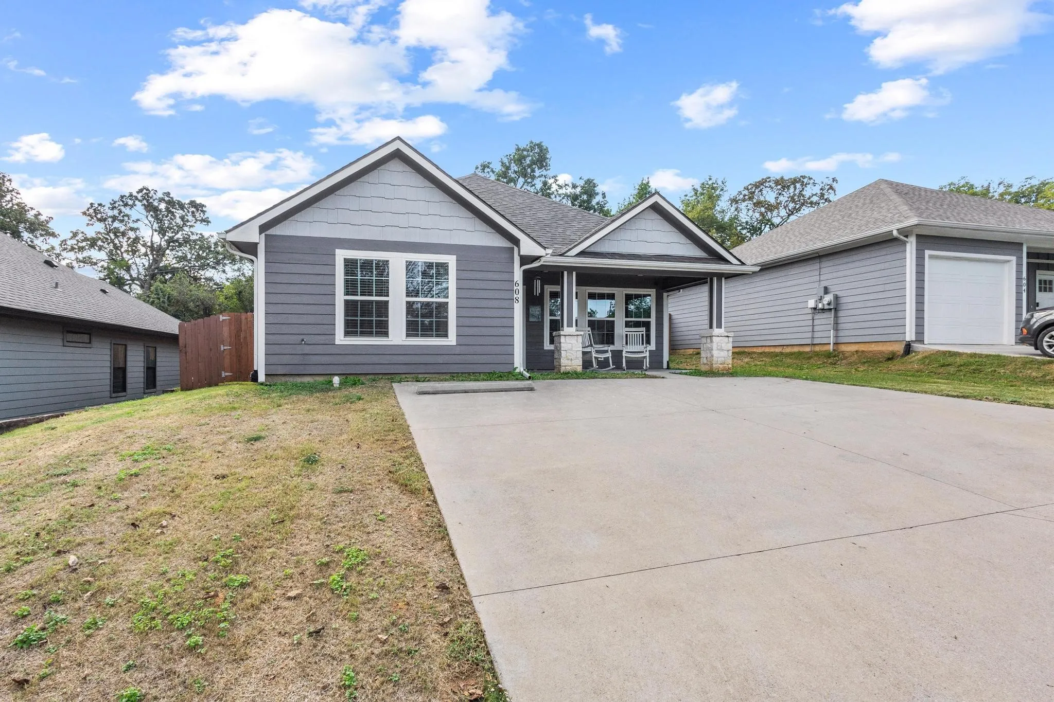 Contemporary home exterior with gray horizontal siding, white trim, and a covered front porch featuring stone-clad pillars