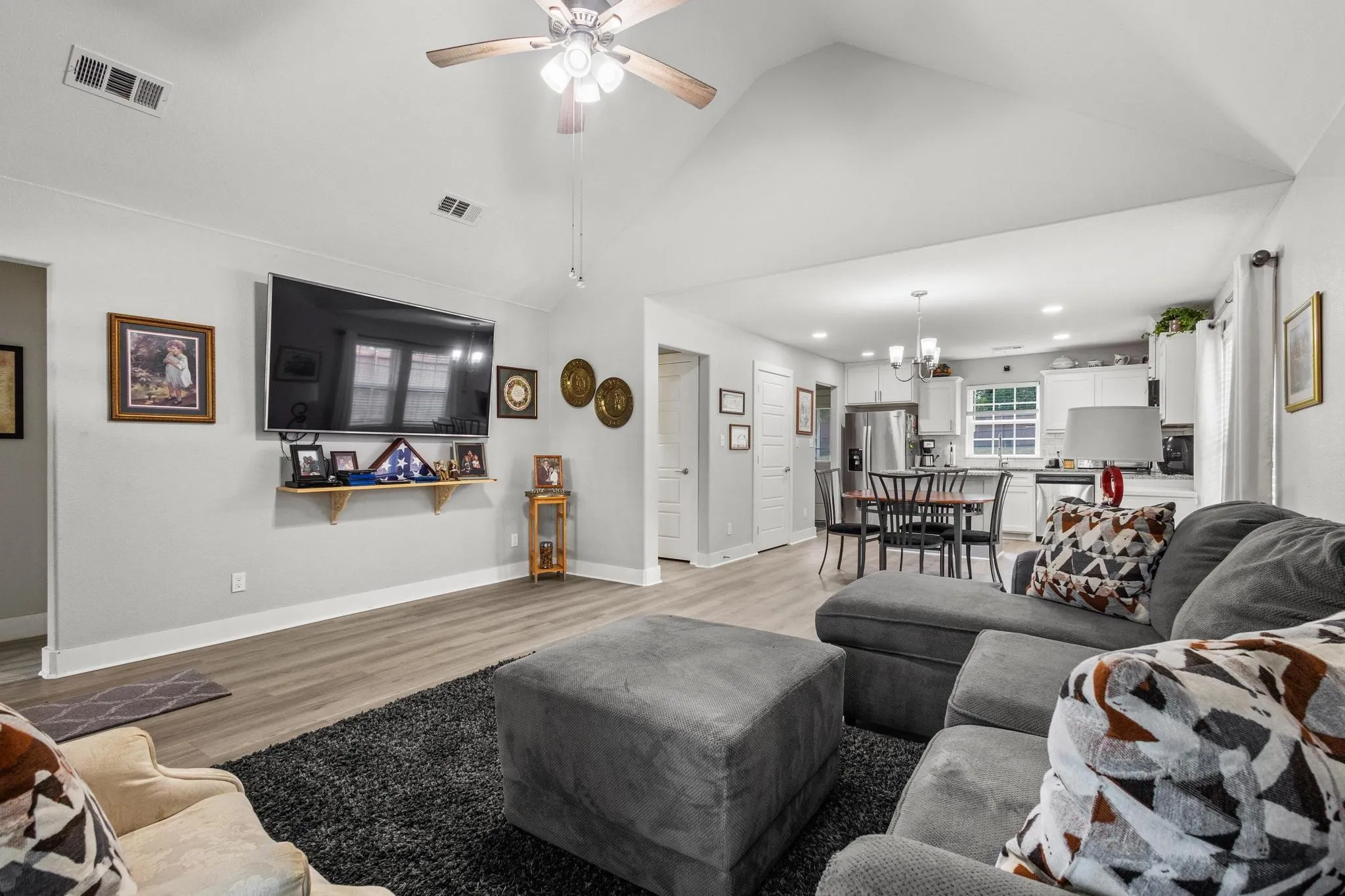 Vaulted ceiling living area featuring wood-finish flooring, a ceiling fan, and a wall-mounted television
