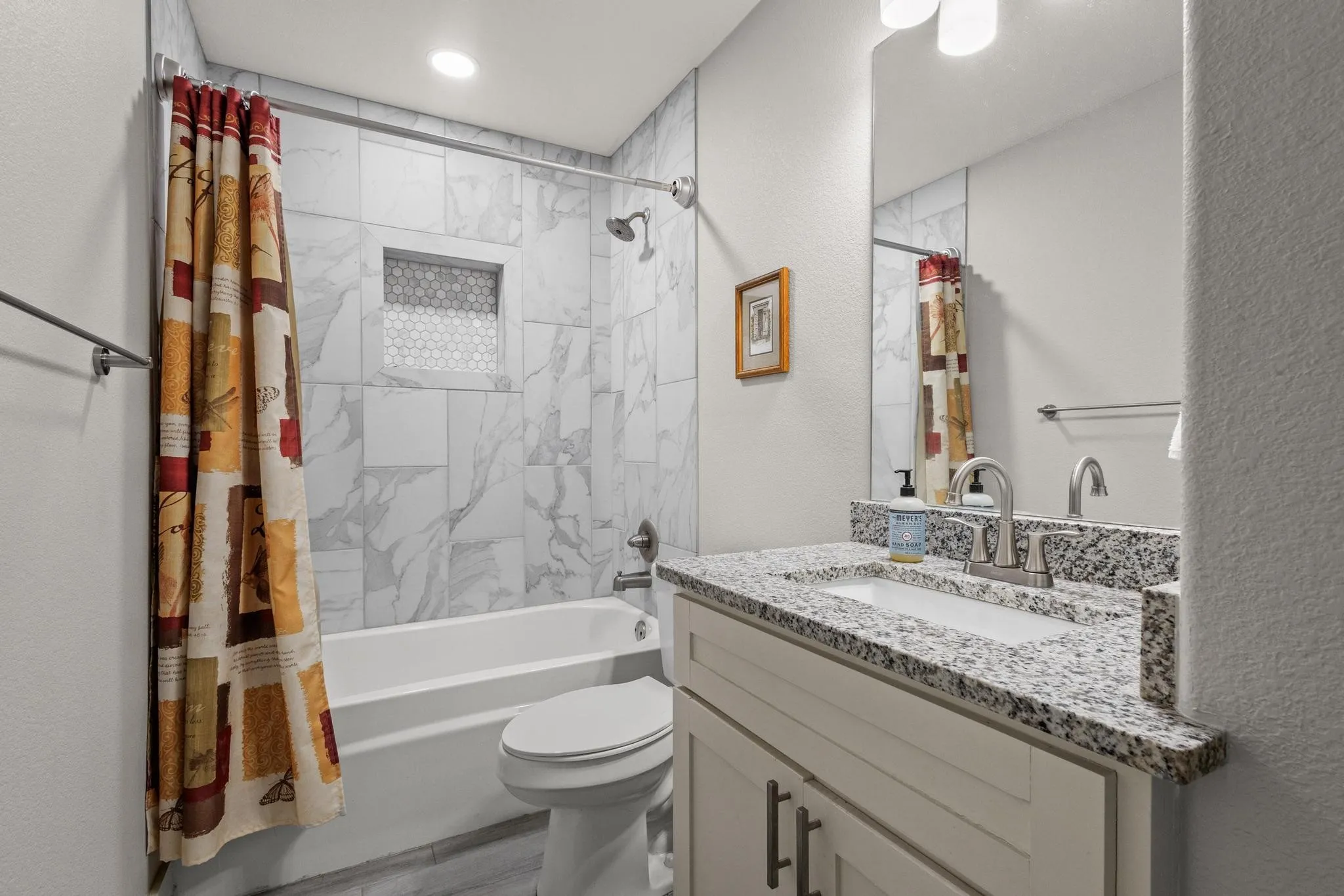 White vanity with granite-style countertop and integrated sink, brushed nickel faucet, and frameless mirror