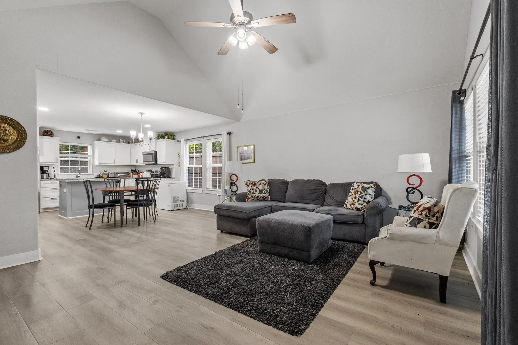 Open-concept living space featuring wood-finish flooring, vaulted ceilings, and a ceiling fan