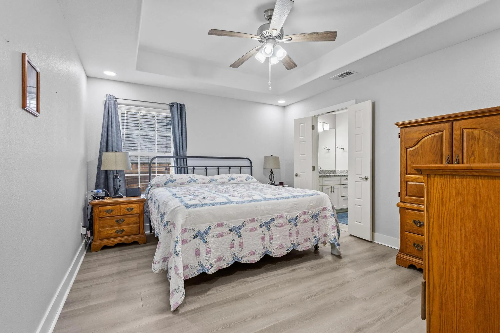 Spacious bedroom featuring wood-finish flooring, a tray ceiling, recessed lighting, and a ceiling fan