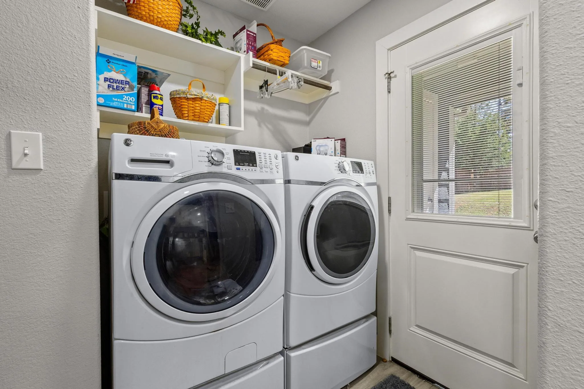Laundry area featuring white appliances, integrated storage shelves, and a paneled exterior door with an inset window and blinds