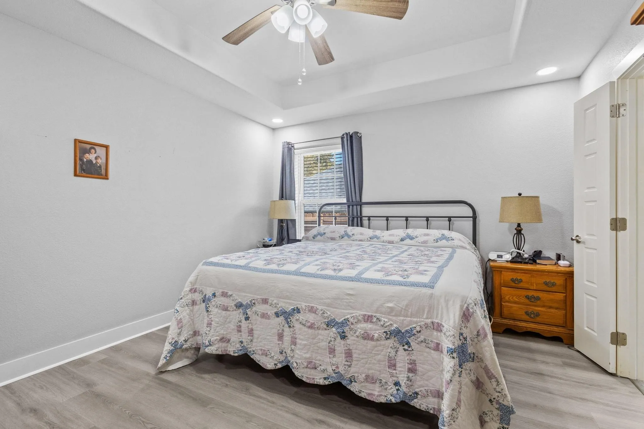 Room featuring wood-finish flooring, a tray ceiling, recessed lighting, a ceiling fan, and a paneled door
