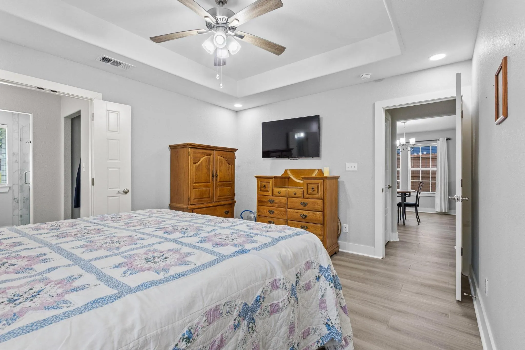 Spacious room featuring tray ceilings with a ceiling fan, recessed lighting, wood-finish flooring, and light gray walls