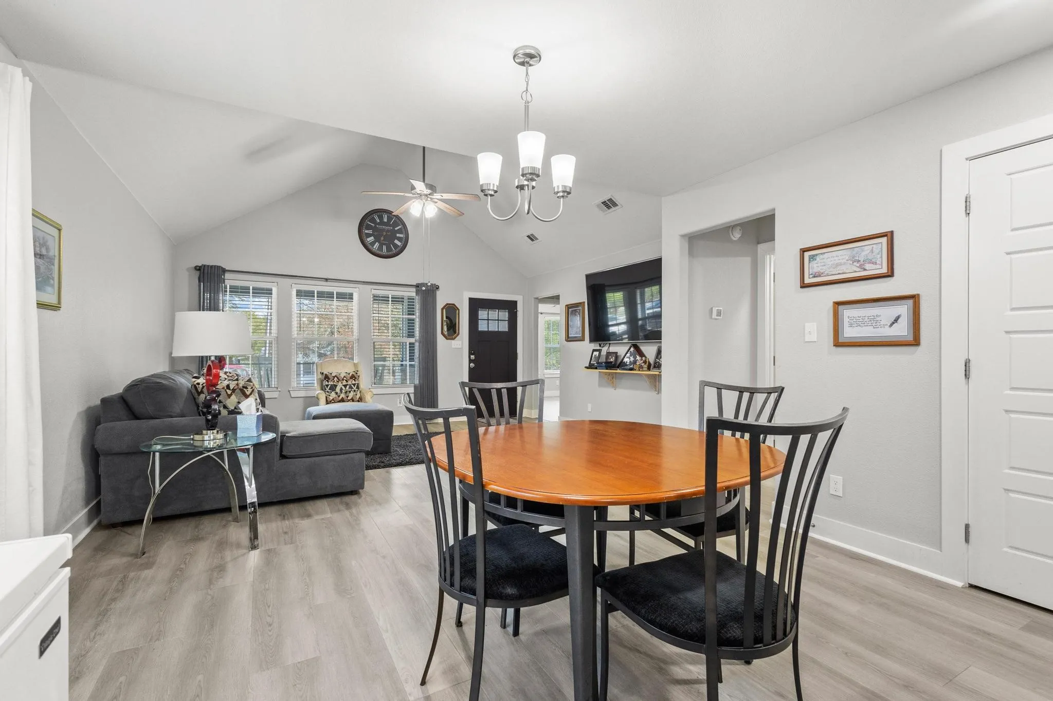 Open-concept living space featuring vaulted ceilings, light wood-finish flooring, a contemporary chandelier, a ceiling fan, and multiple large windows