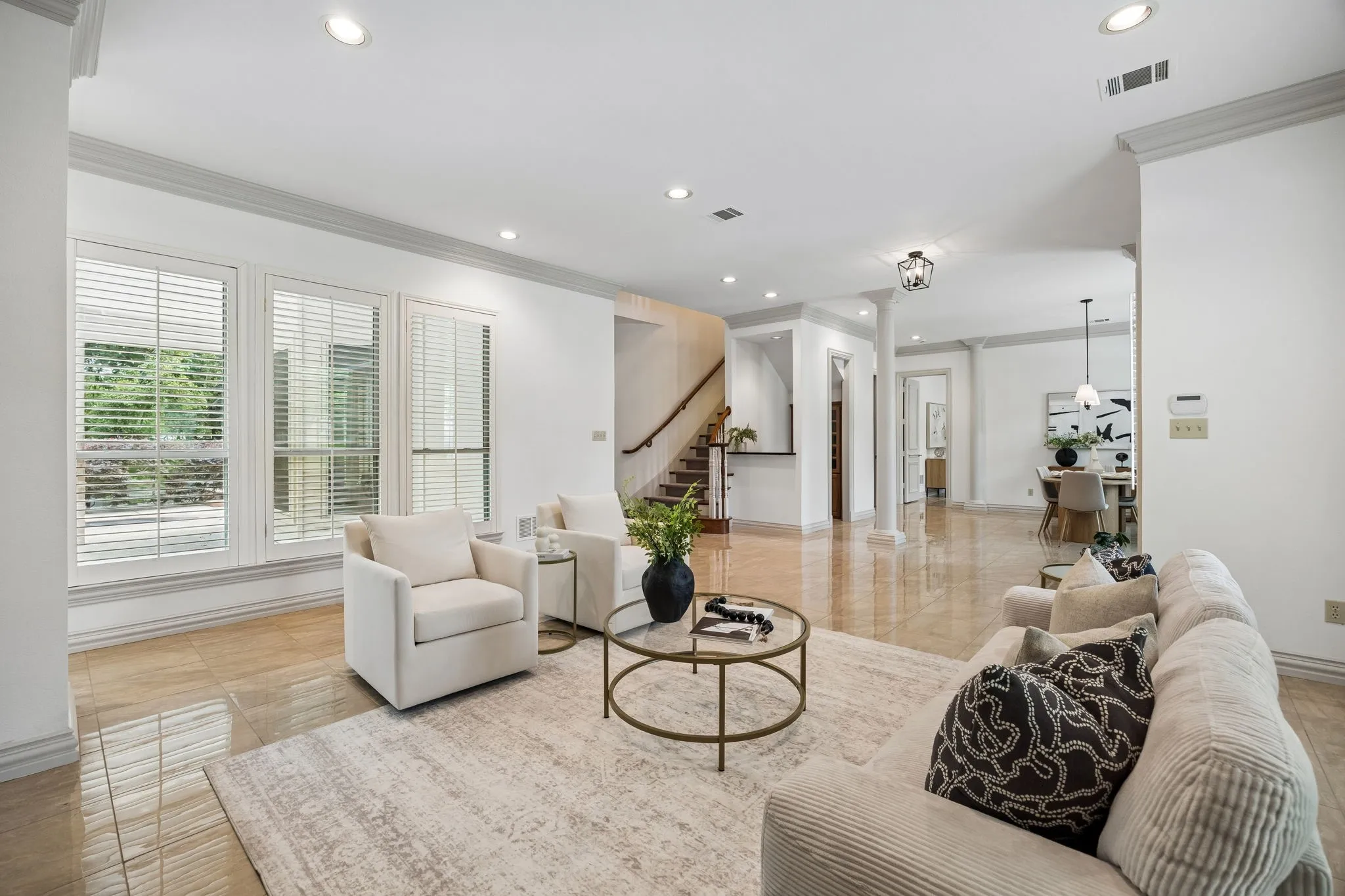 Spacious living area featuring polished tile flooring, recessed lighting, crown molding, and large windows with horizontal blinds