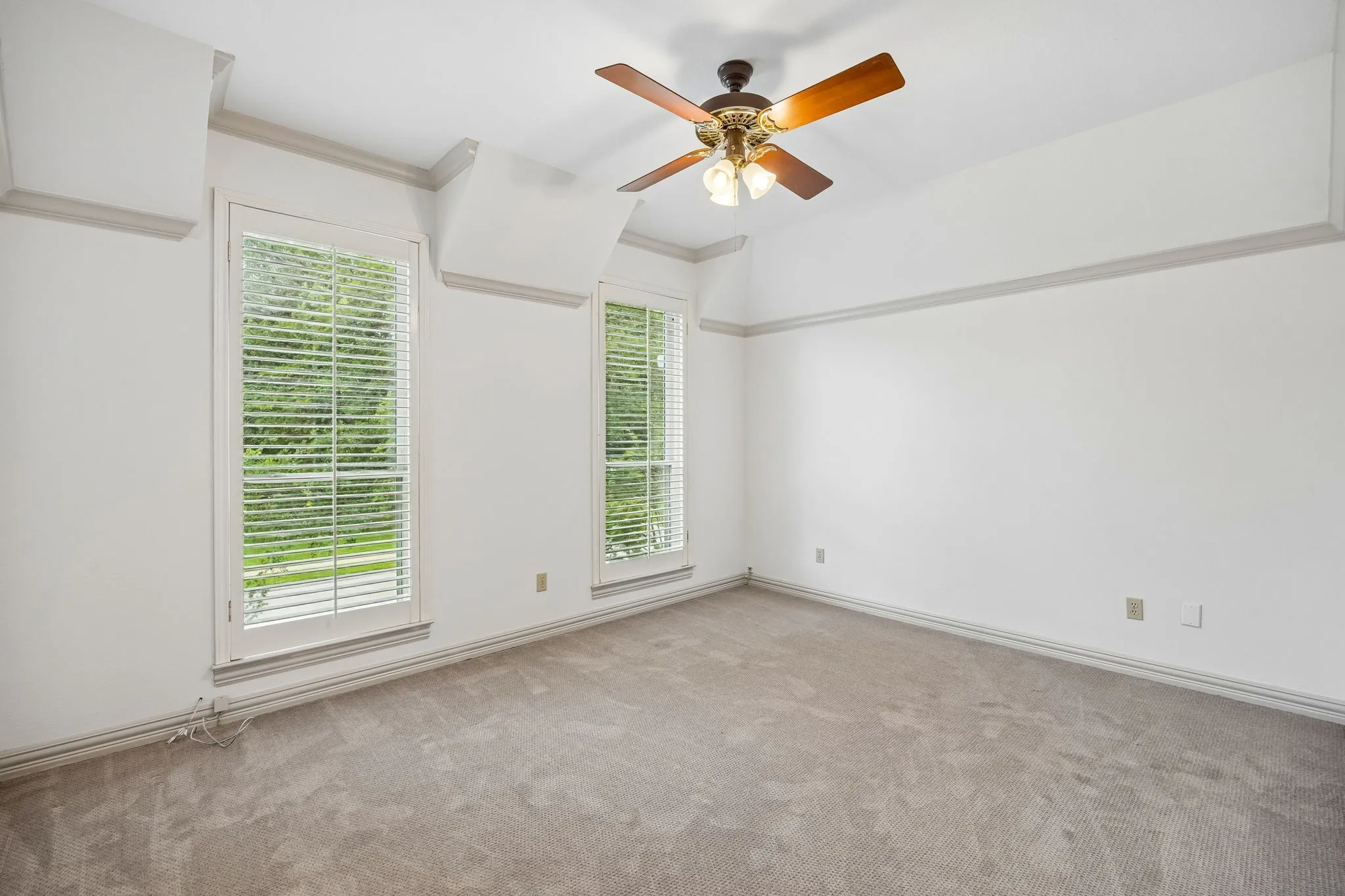 Spacious room featuring two large windows with white louvered blinds, crown molding, and a ceiling fan with light fixture