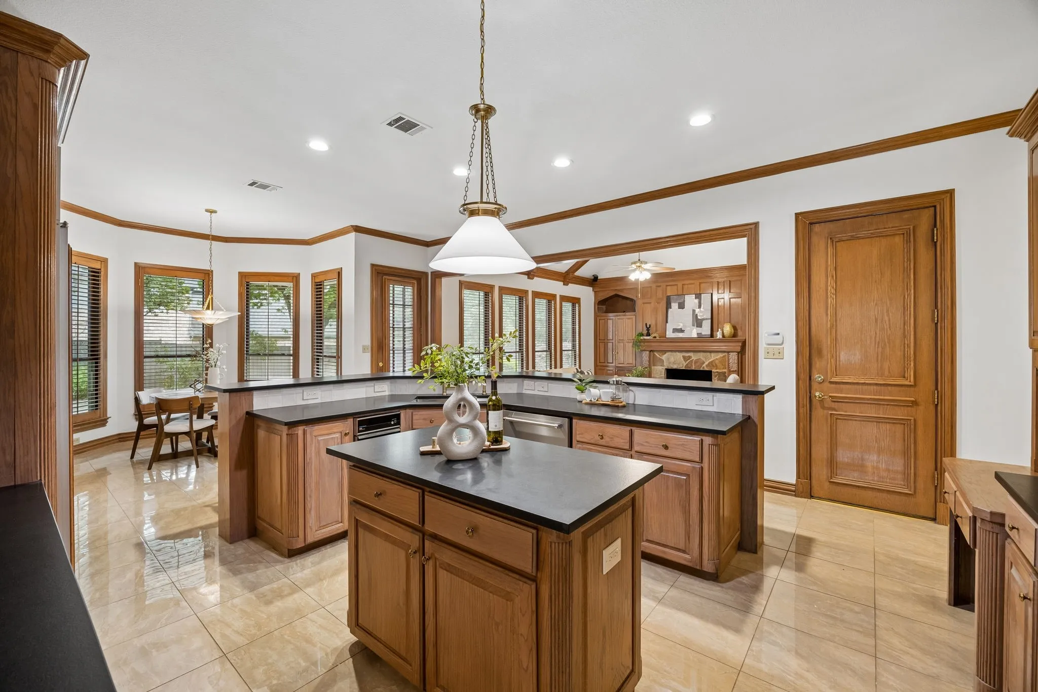 Spacious kitchen featuring a central island, extensive wood cabinetry, dark countertops, and tile flooring